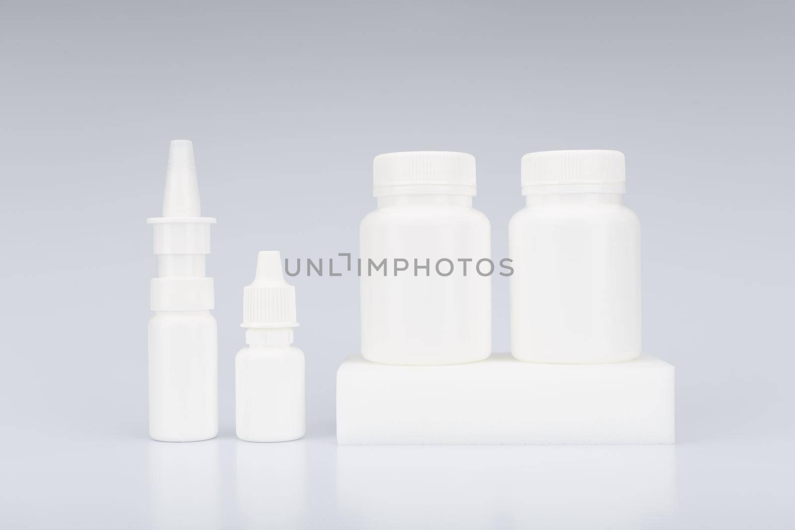 Simple still life with nose spray, eye drops and two white unbranded medication bottles on podium against light grey background. High quality photo