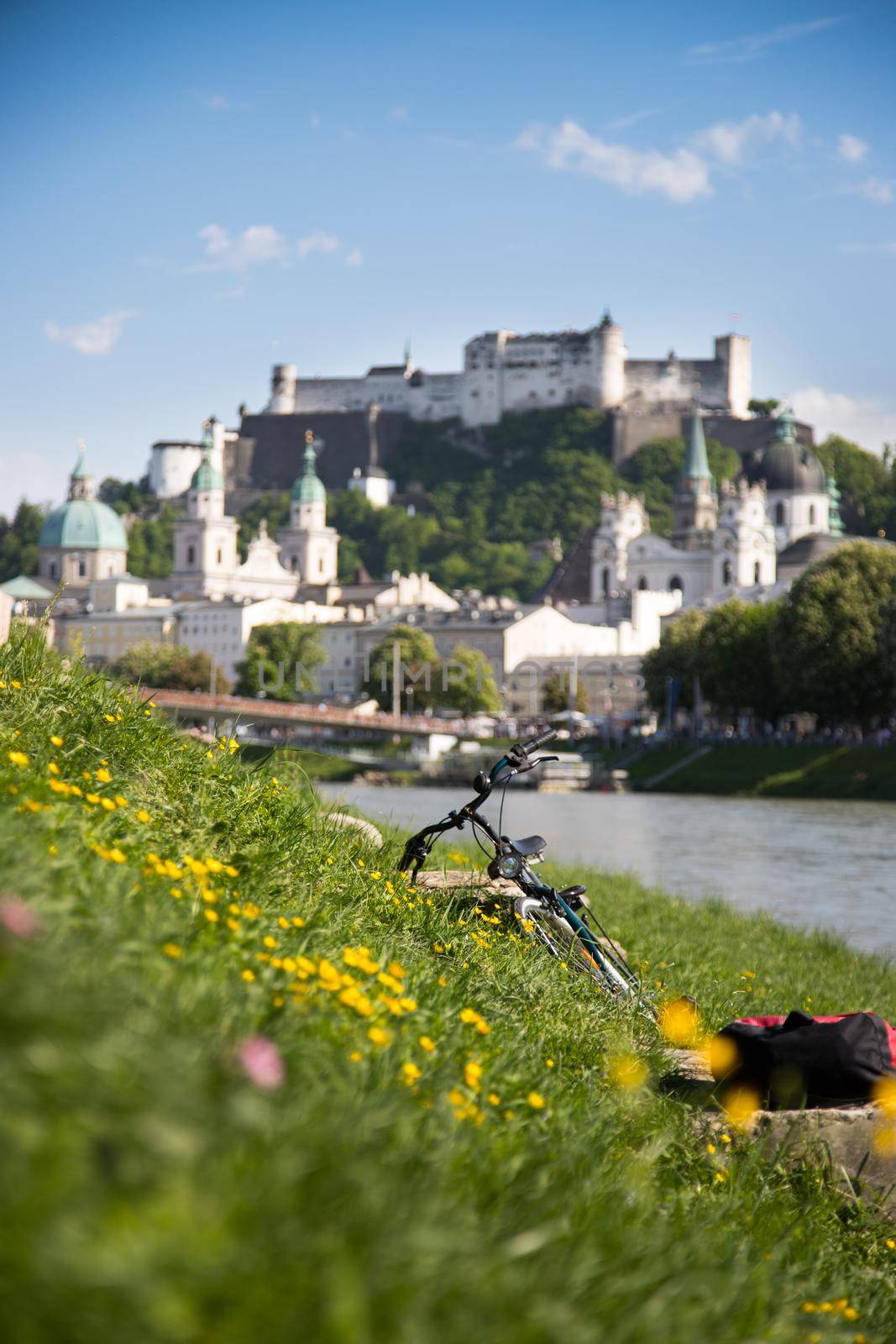 Salzburg summer time: Panoramic city landscape with Salzach with green grass and historic district. Bicycle in the foreground. by Daxenbichler