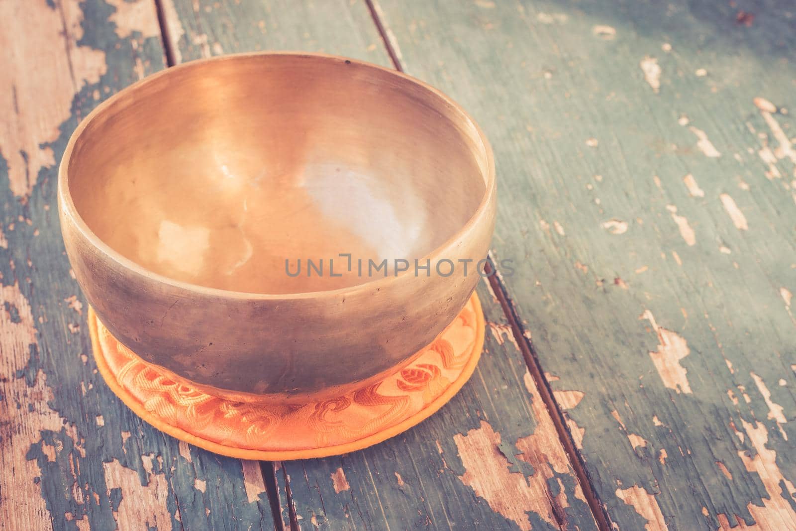 Metal singing bowl on a rustic green, wooden table outdoors. Flowers in the colourful, blurry background