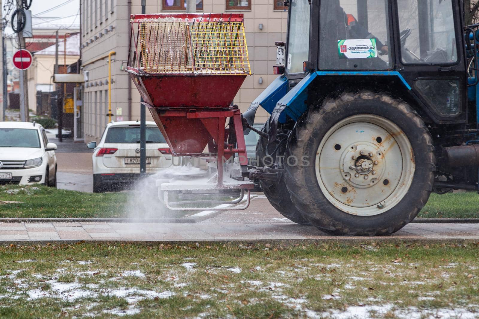 TULA, RUSSIA - NOVEMBER 21, 2020: Tractor spreading salt reagent over city pavement at winter daylight.