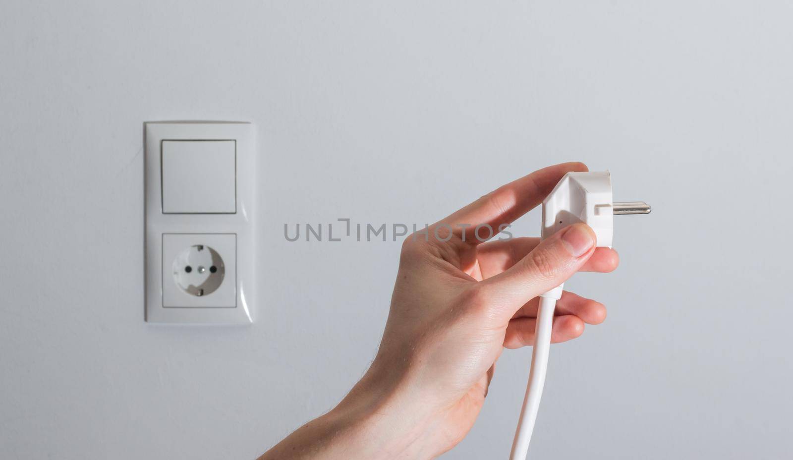 White plug with cable in males hand, ready to connect. Energy concept.