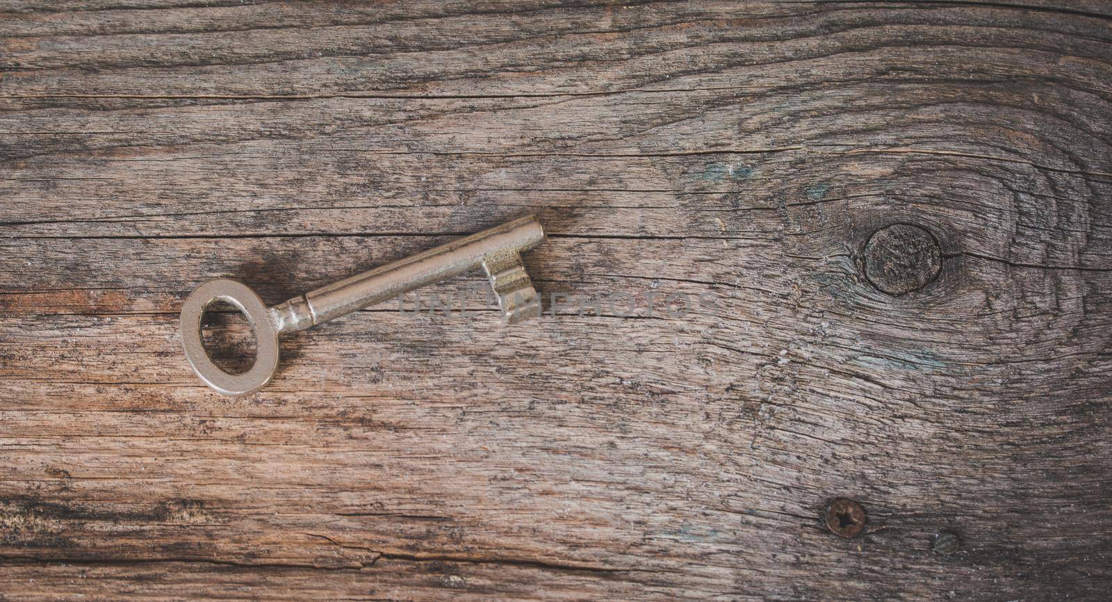 Old key is lying on a rustic wooden desk