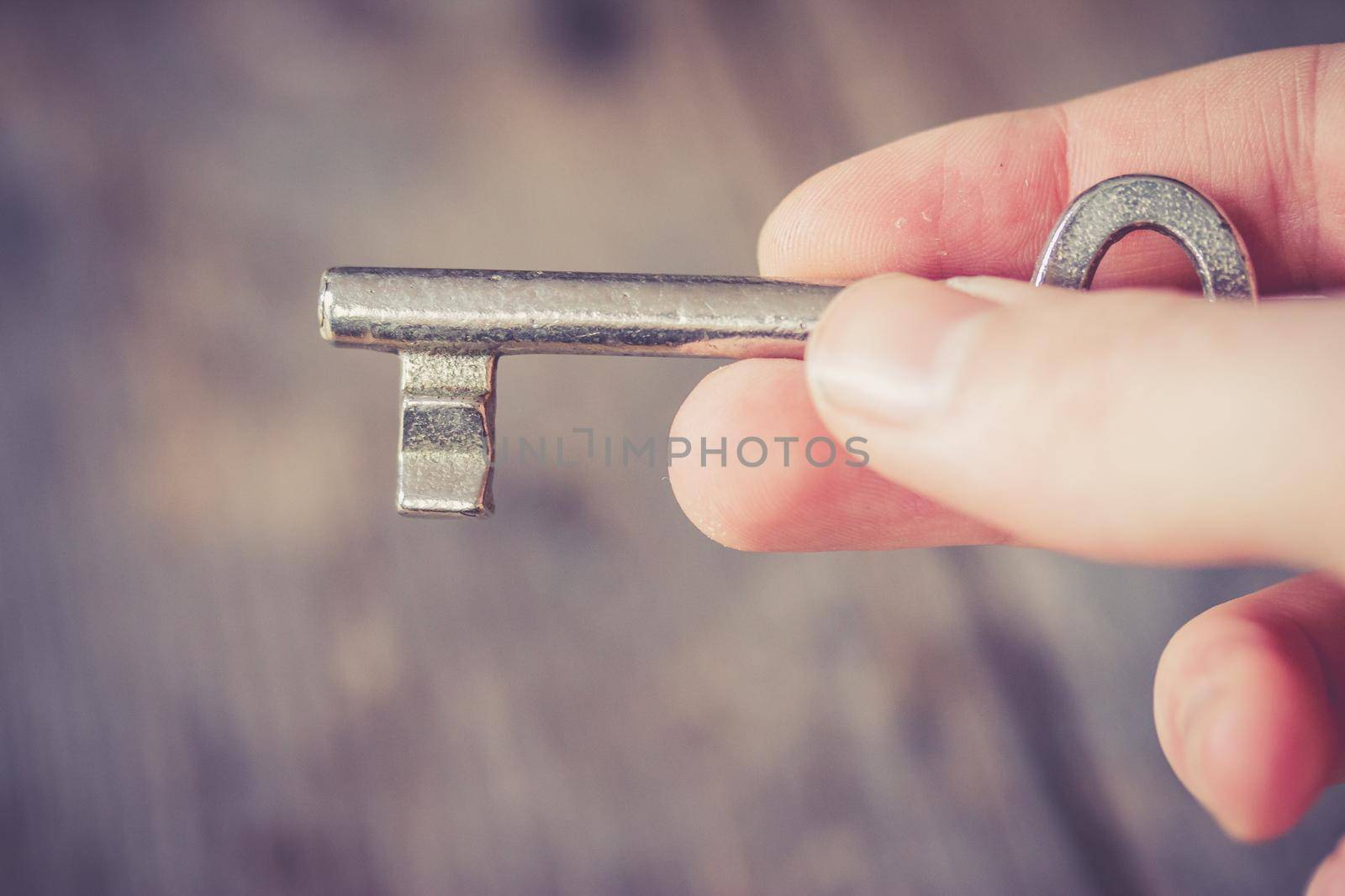 Young male hand is holding and old key, wooden desk in background