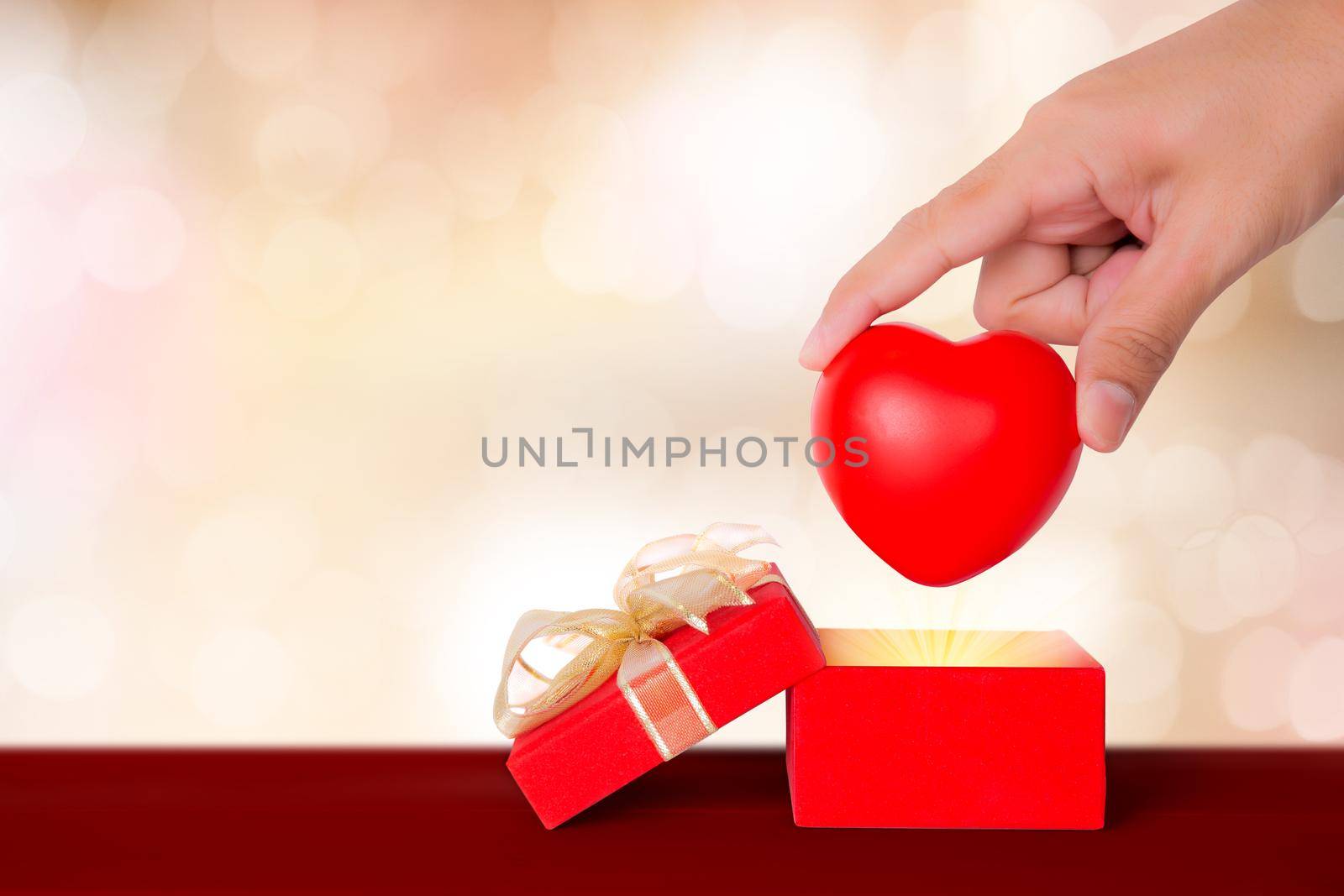 Valentine day, hand put heart shape in red gift box on wooden bokeh background, celebration and anniversary with giving love, presents with romantic and surprise, holiday and festive concept.