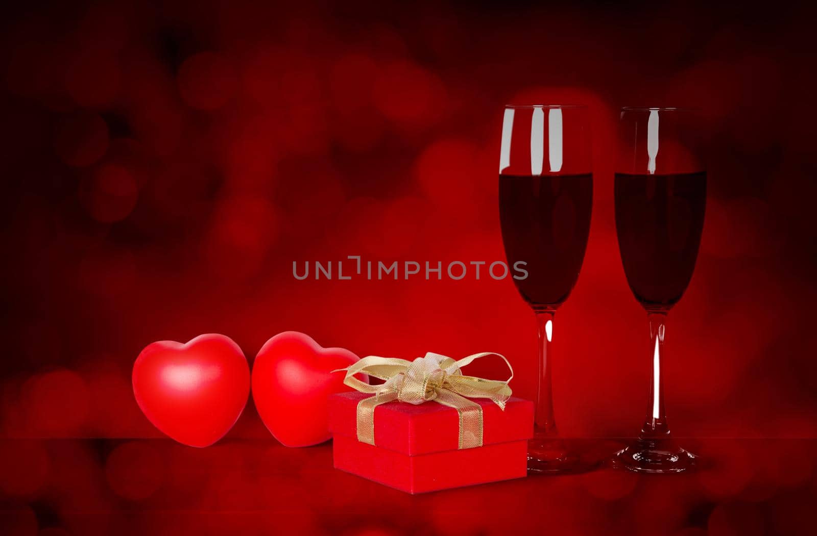 Two wineglasses and red gift box and heart shape on desk with red blur bokeh background, champagne glasses and presents with celebration and anniversary, love and romantic, valentine day concept.