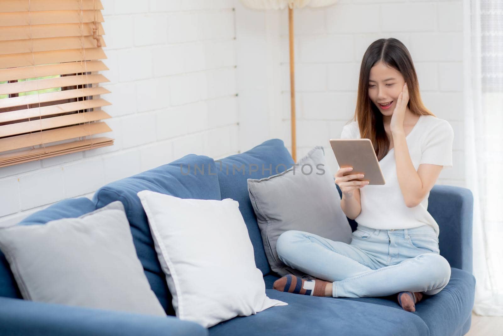 Young attractive asian woman resting using browsing tablet computer on sofa at home, happy girl sitting on couch relax reading digital gadget with excited, communication and lifestyle concept.