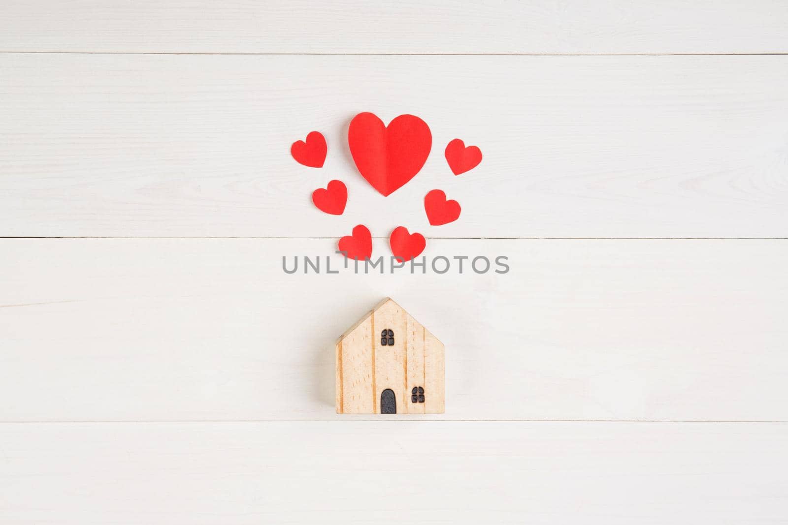 Wood house with heart shape paper on white wooden desk background, love and harmony of family, residence and insurance, symbol and sign, top view, flat lay, copyspace, nobody.
