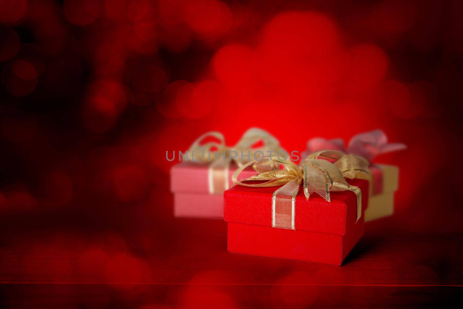 Red gift box with ribbon and light blurred bokeh background, present with luxury for love and anniversary with glowing and sparkle in festive, copy space, Valentine day or Christmas concept.