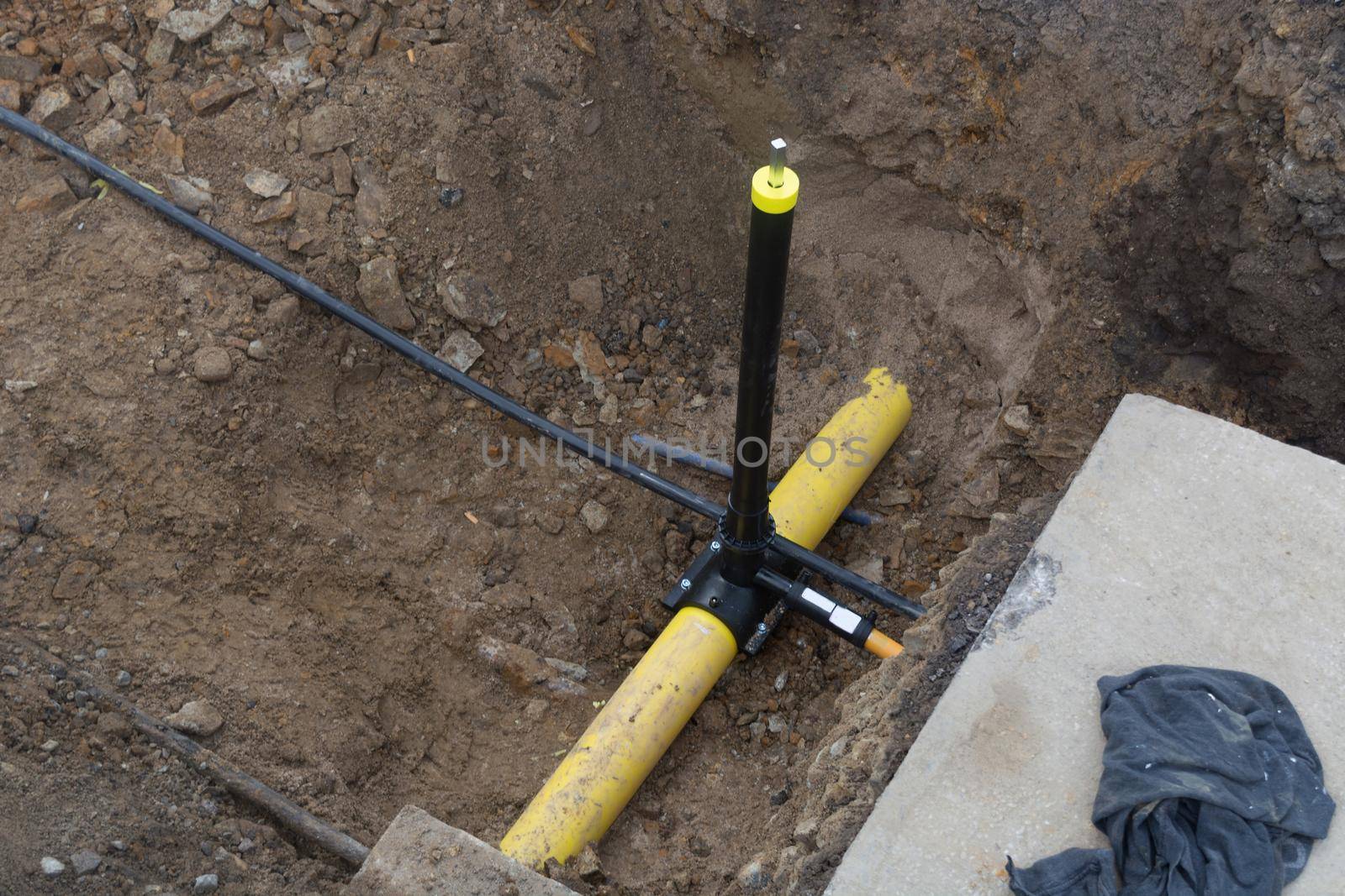 Work on the installation of engineering and heating systems. Two plastic pipes one yellow for gas pipe and one black for power lines. They are in a sand ditch.