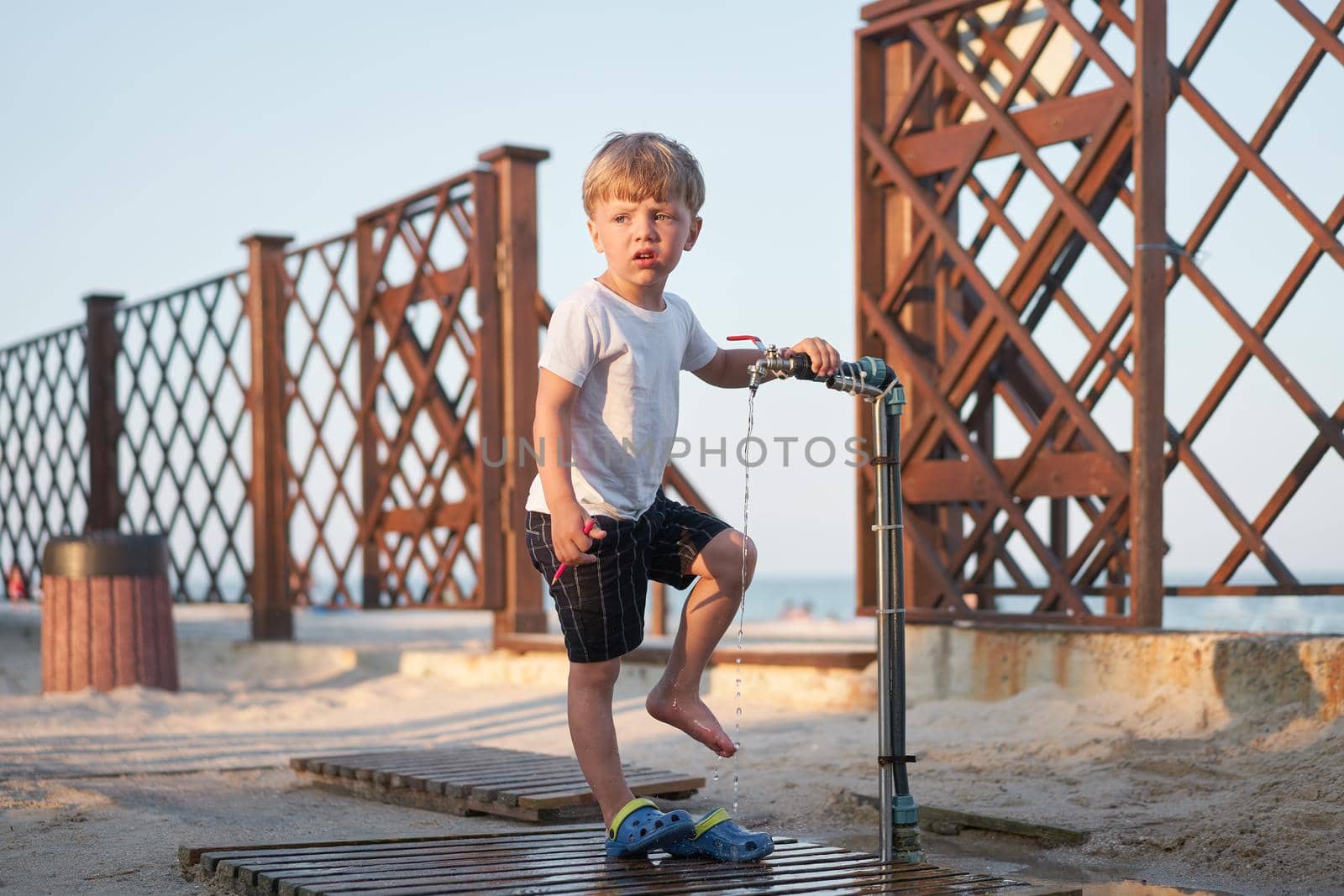 Child wash legs after beach sand Caucasian boy standing beach. Childhood summertime. Family vacation with one child.