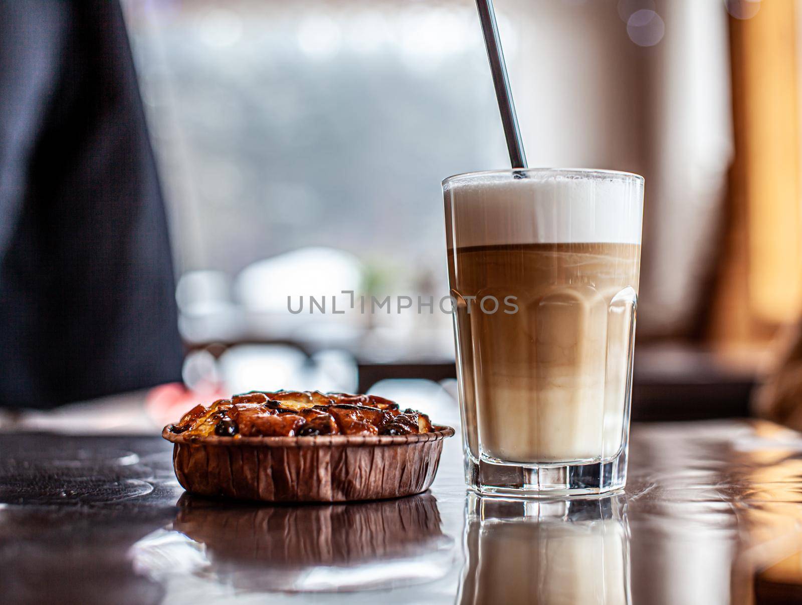 Hot Latte coffee in a glass and a fresh apple dessert next to it. The hot drink is served with a plastic straw. Delicious breakfast in the cafe