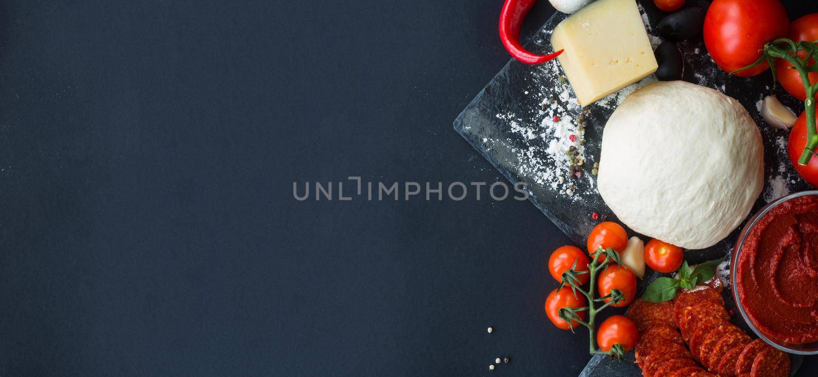 Raw dough for pizza with ingredients and spices on black table background with copy space for text