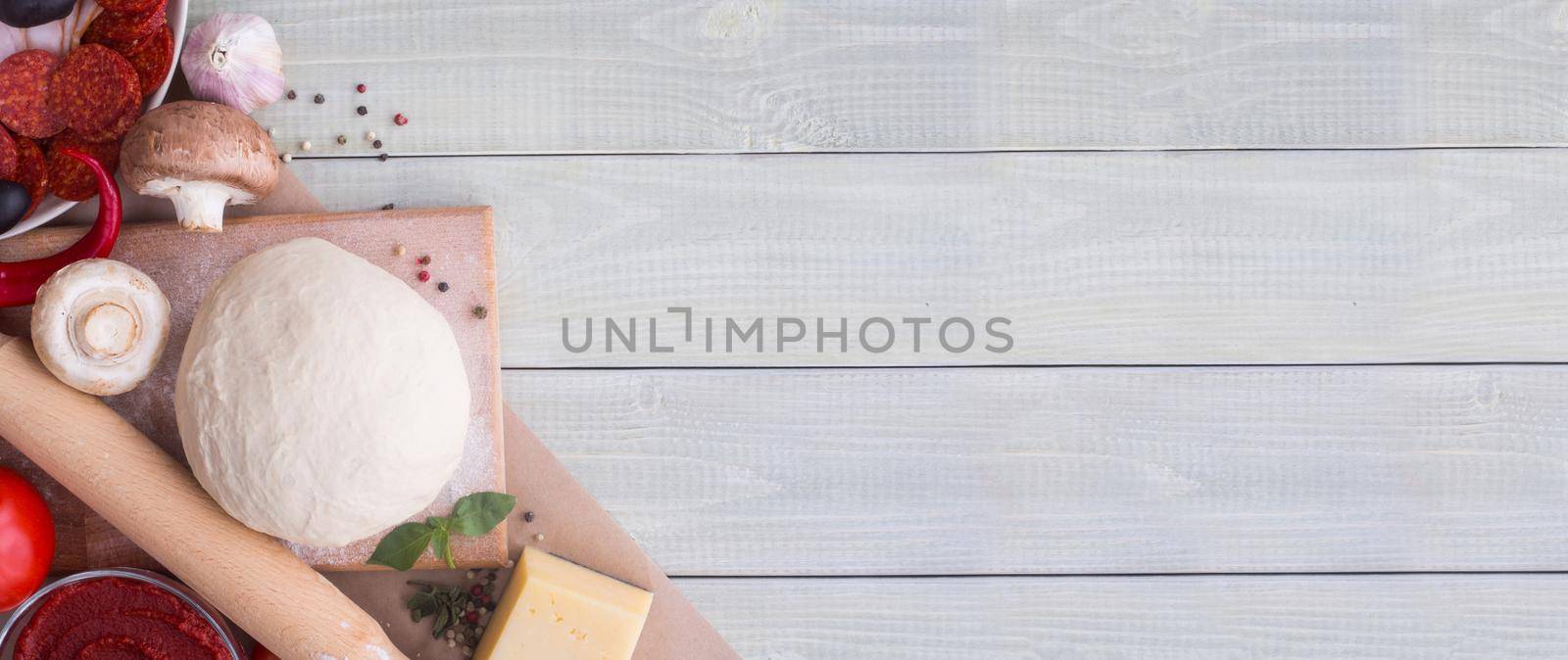 Raw dough for pizza with ingredients and spices on white wooden table background