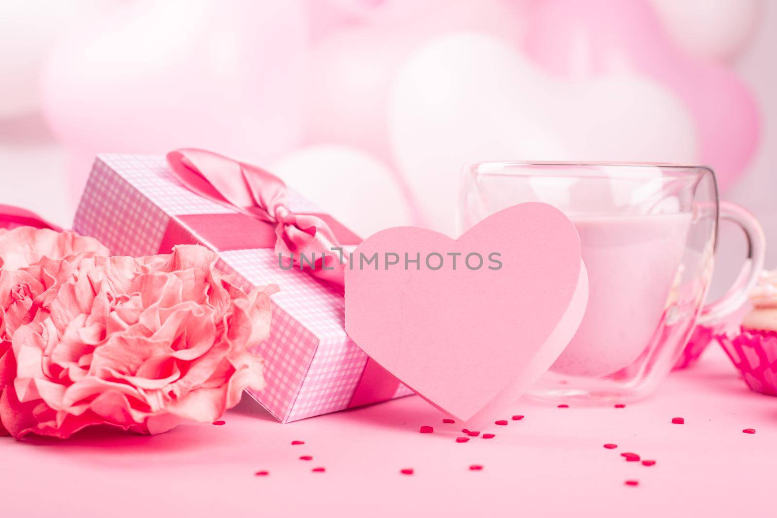 Valentine Day gift in a box wrapped in striped paper and tied with silk ribbon bow and dessert on pink balloons background with copy space for text