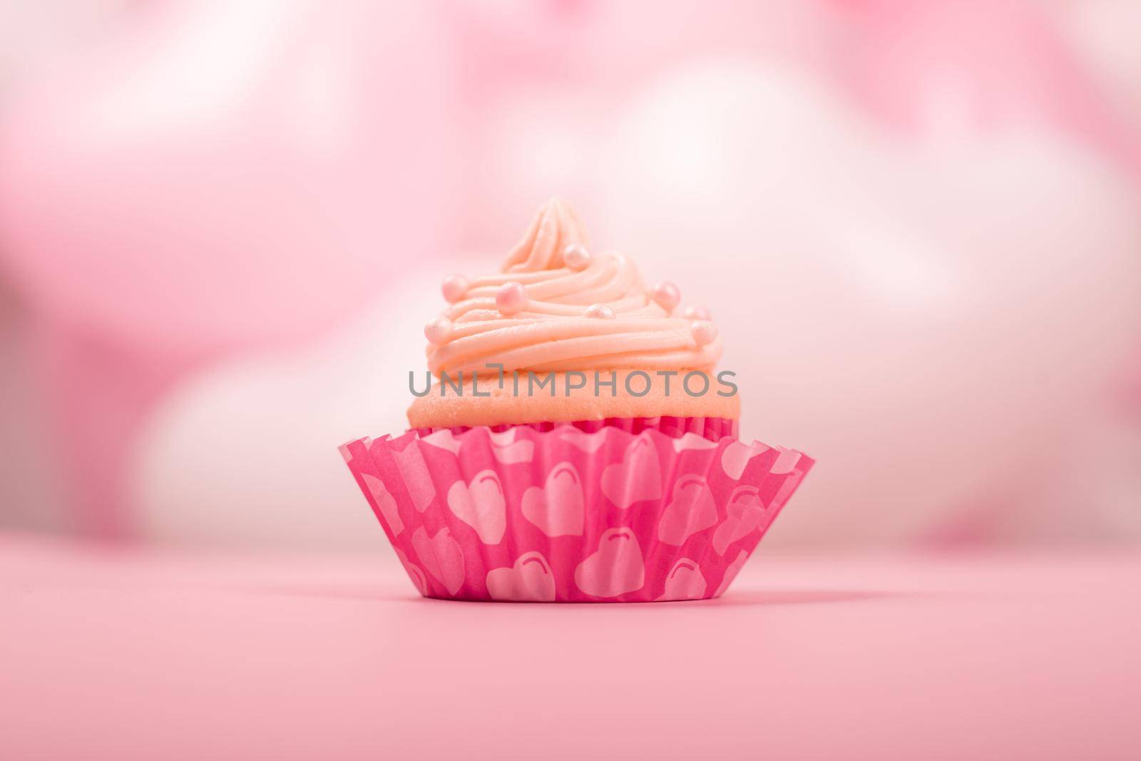Valentine day love cupcake decorated with cream on pink and white party heart balloons background with copy space for text