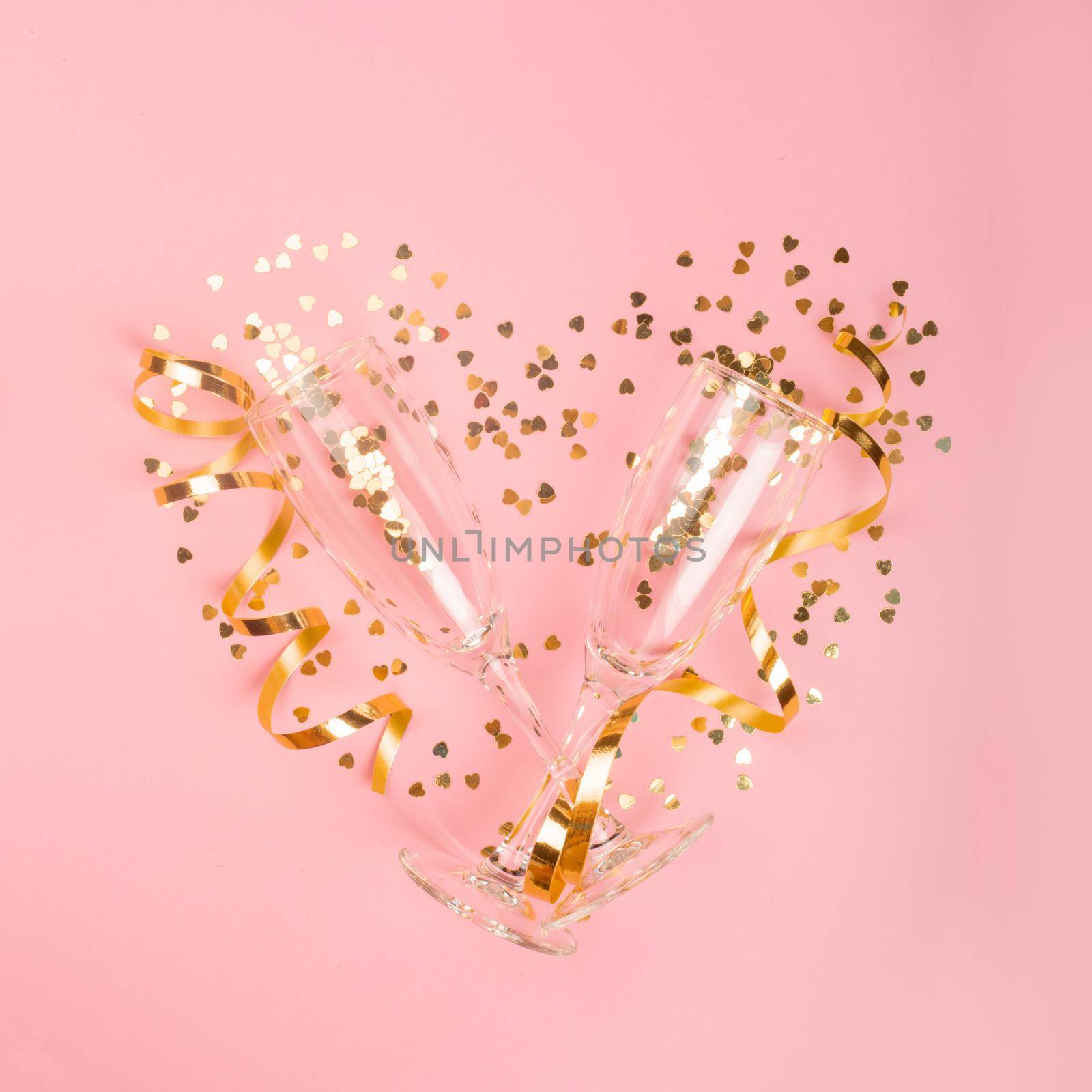 Valentines day champagne flutes glasses and heart shaped golden glitters on pink background with copy space for text