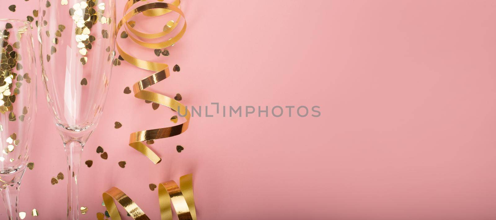 Valentines day champagne flute glasses and heart shaped gold glitters on pink background with copy space for text