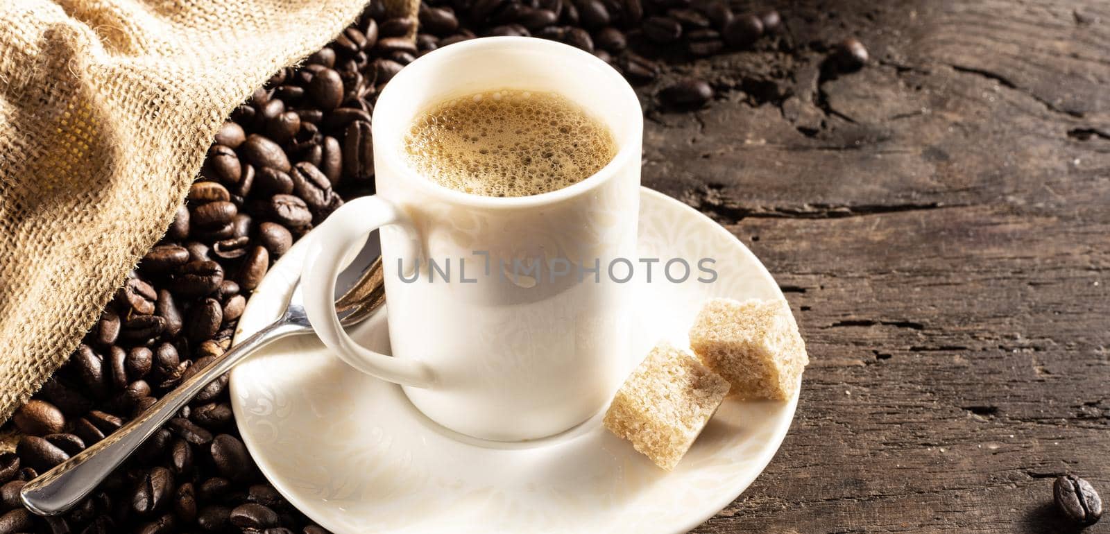 Rustic background with cup of coffee espresso in white porcelain cup with roasted coffee beans on old wood background with canvas bag