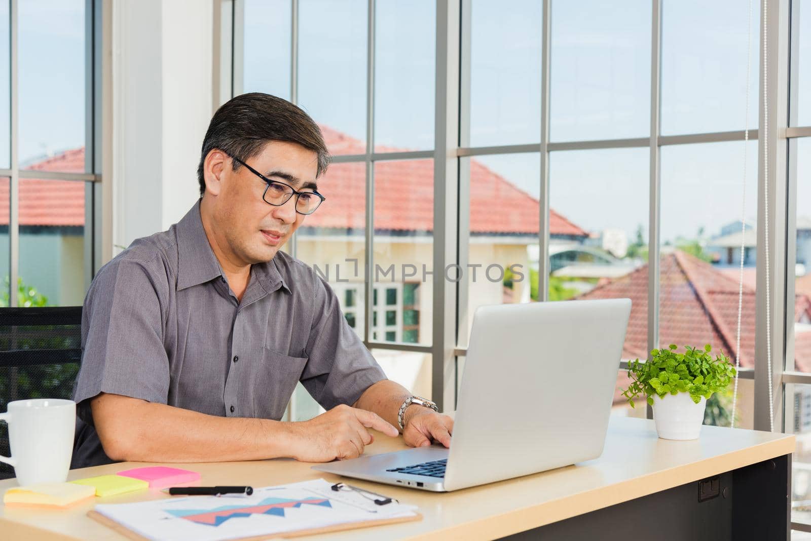 Asian senior business man working online on a modern laptop computer he looking at the screen for remote online studying. Old businessman people using the laptop to video call conference on desk table