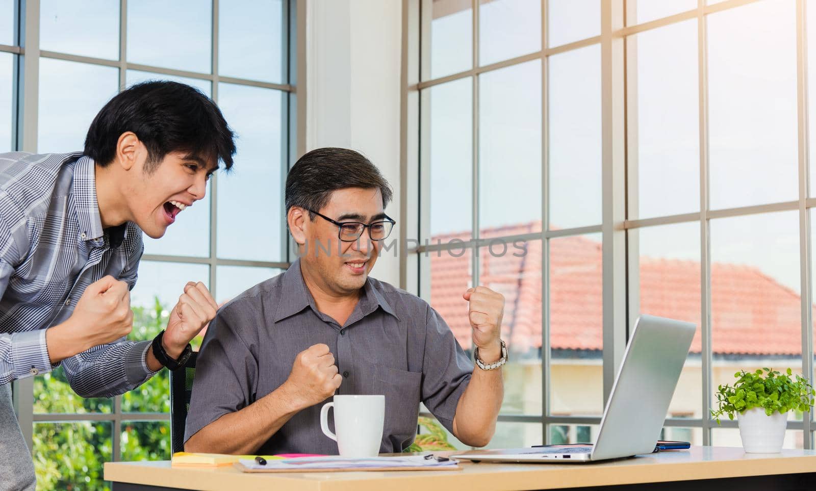 Asian senior and young business man people excited celebrating corporate victory together in office. Happy old and junior two businessmen video call conference on laptop computer success win triumph