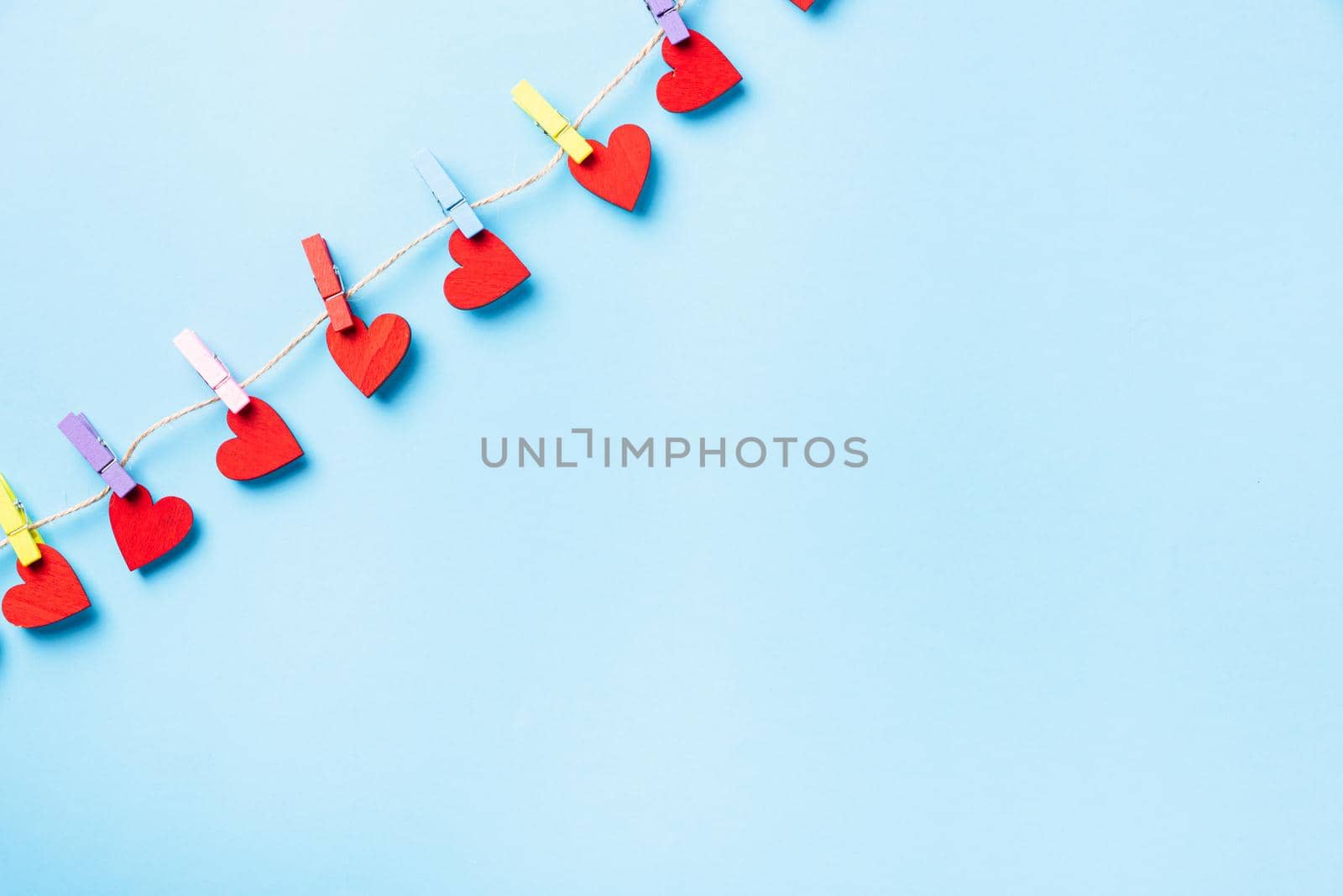 Valentine's day concept. red heart-shaped valentines decoration hanging with wood clips for happy love on the rope greeting card isolated on blue background with copy space