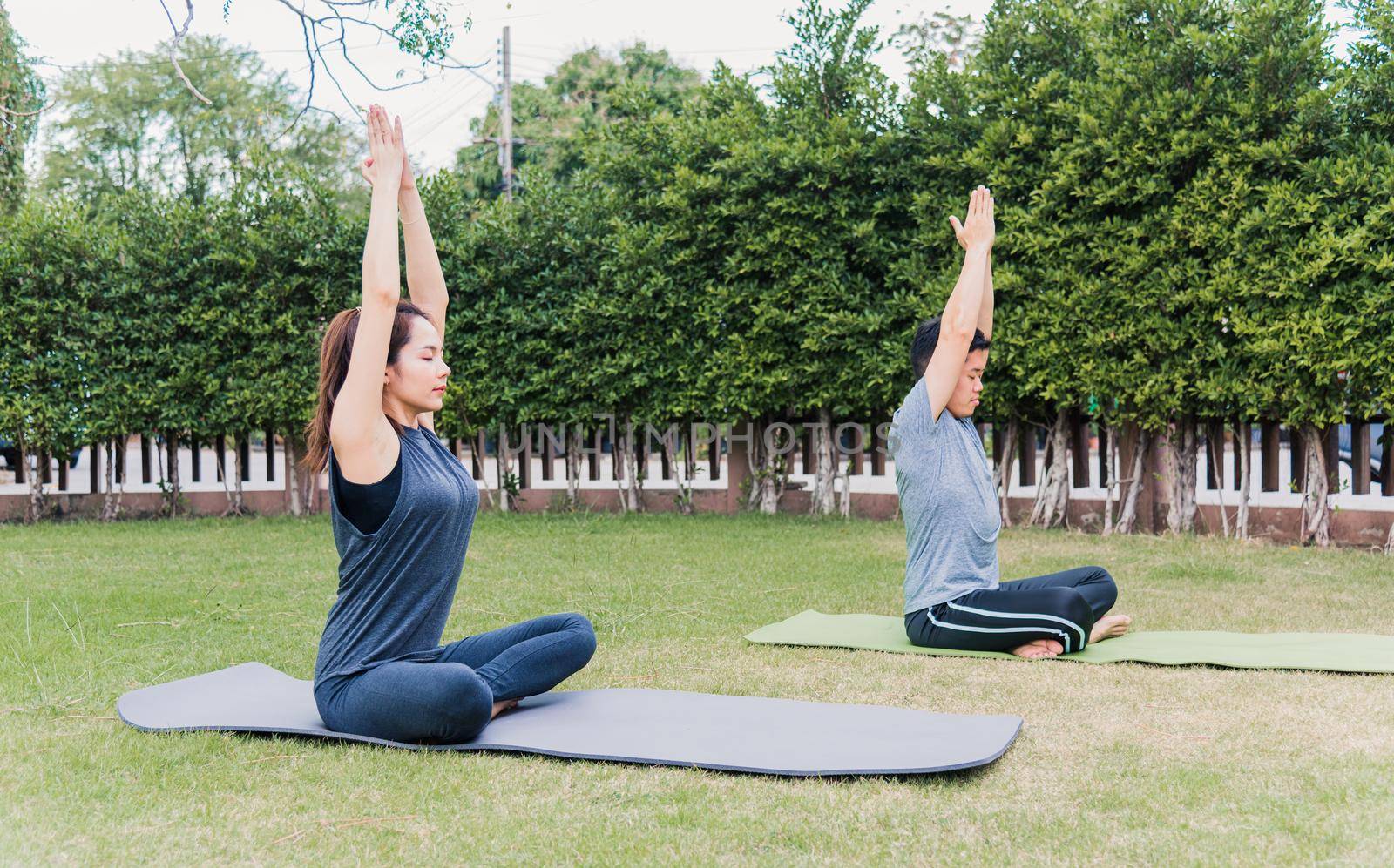 man and woman practicing doing yoga outdoors in meditate pose sitting on green grass by Sorapop