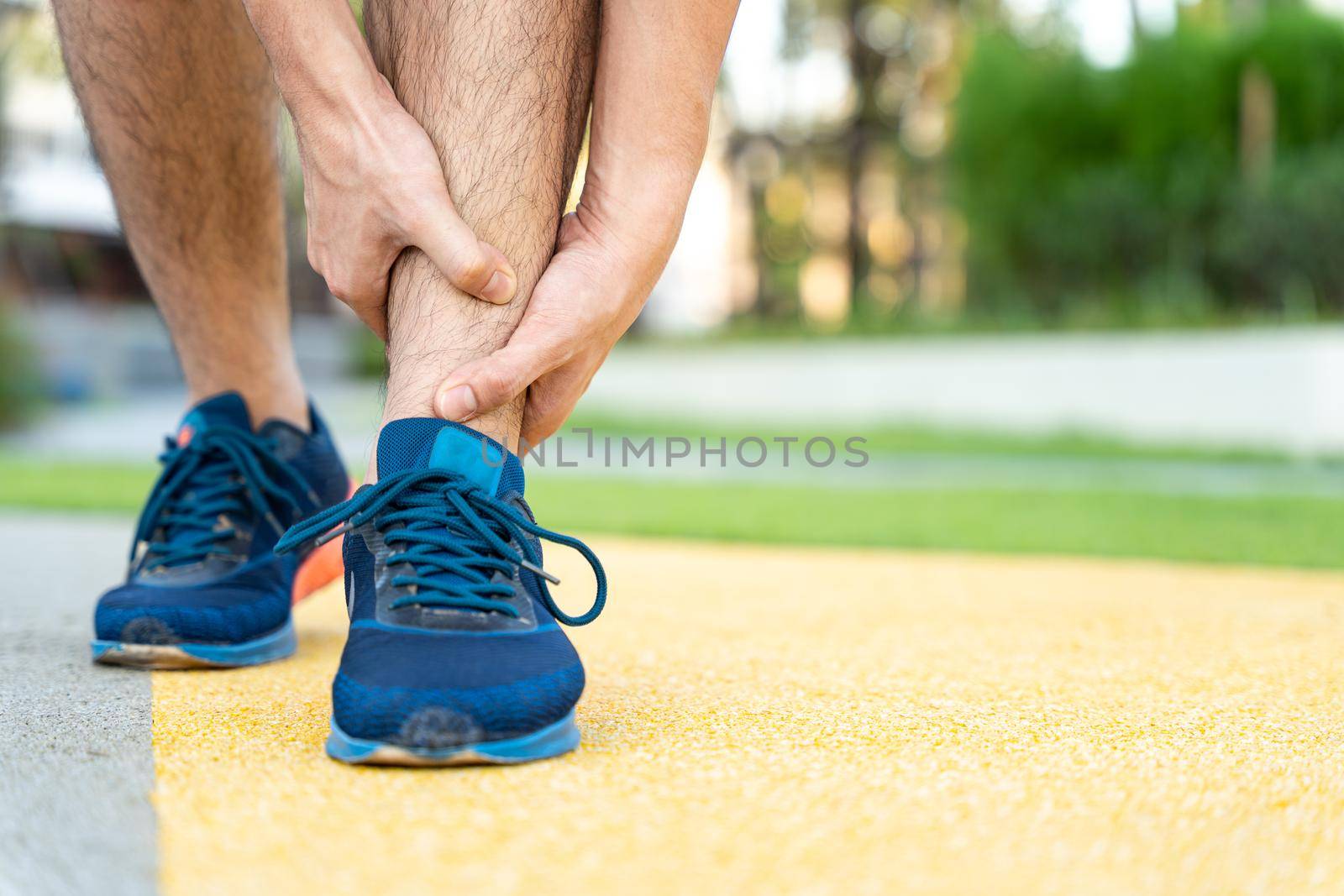 Male runner athlete leg injury and pain. Hands grab painful leg while running in the park.