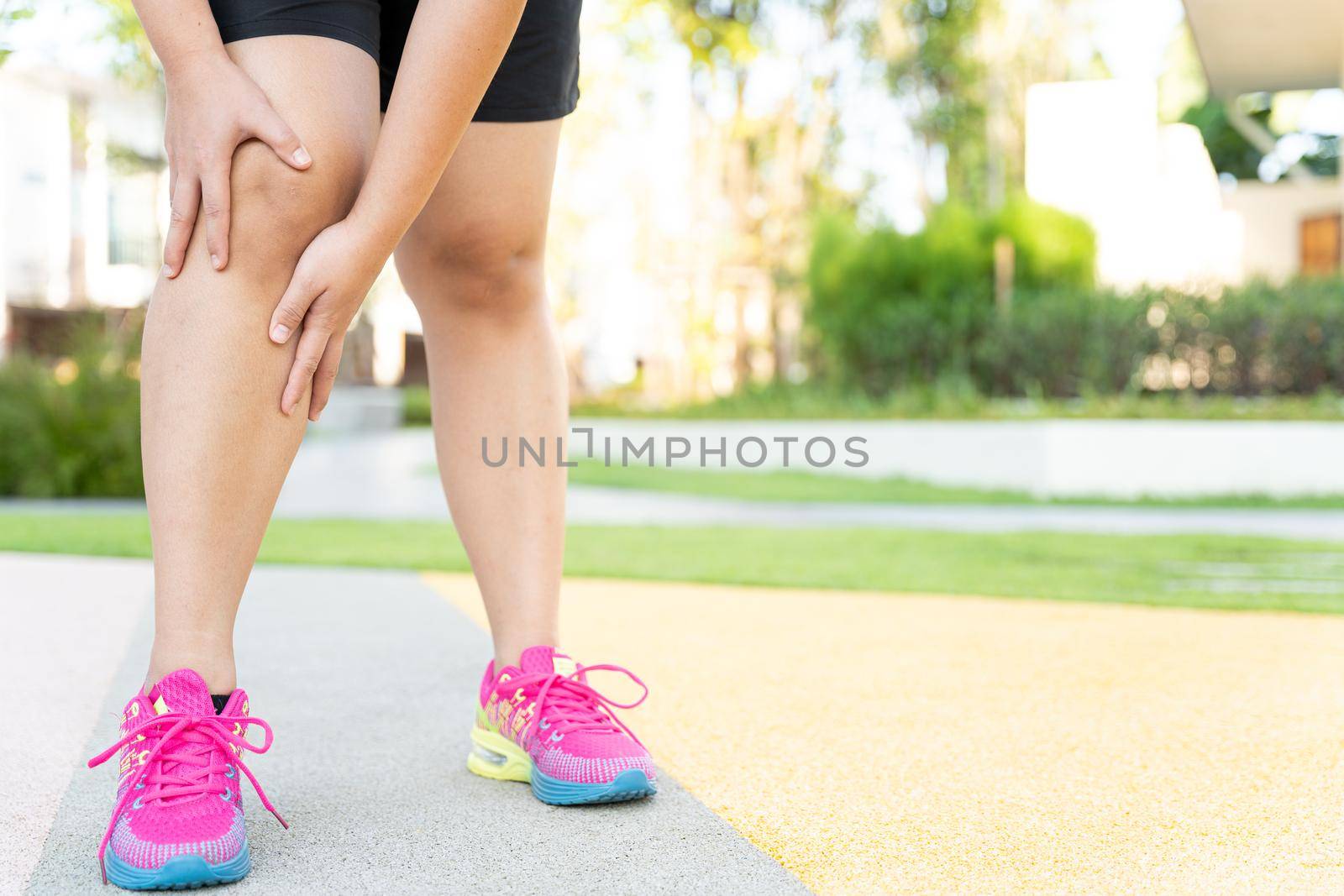 Female fatty runner athlete leg injury and pain. Hands grab painful knee while running in the park.