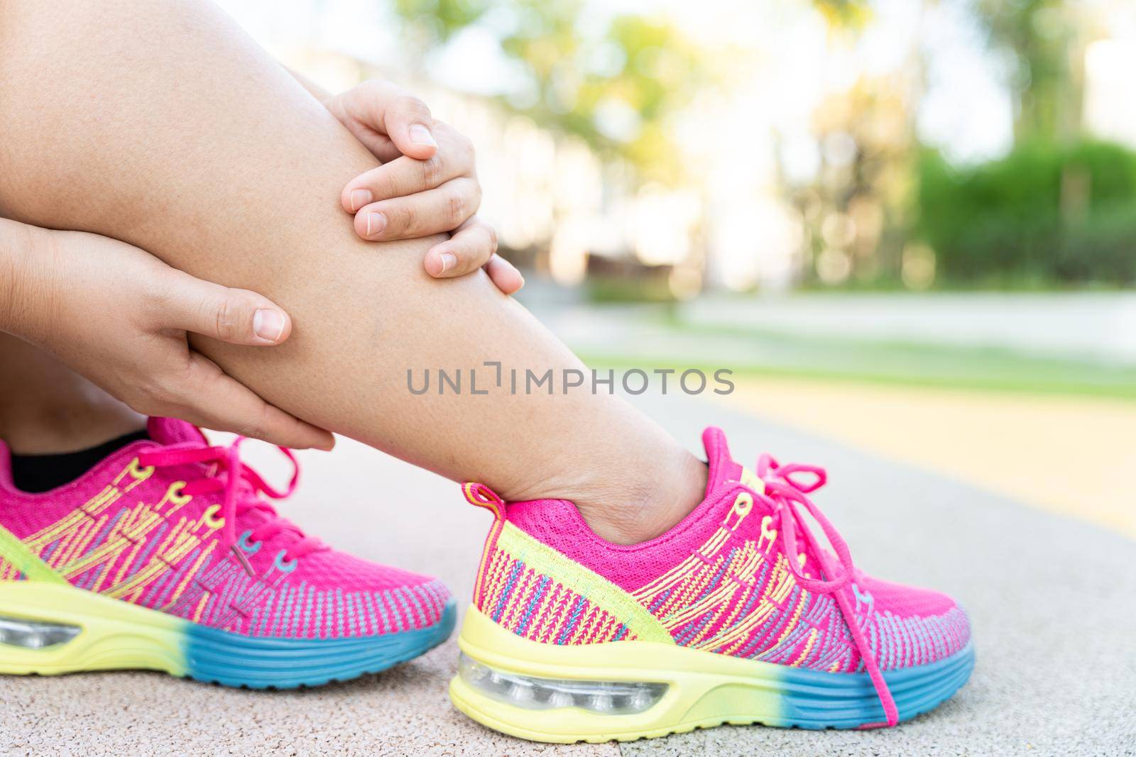 Female fatty runner athlete leg injury and pain. Hands grab painful leg while running in the park.