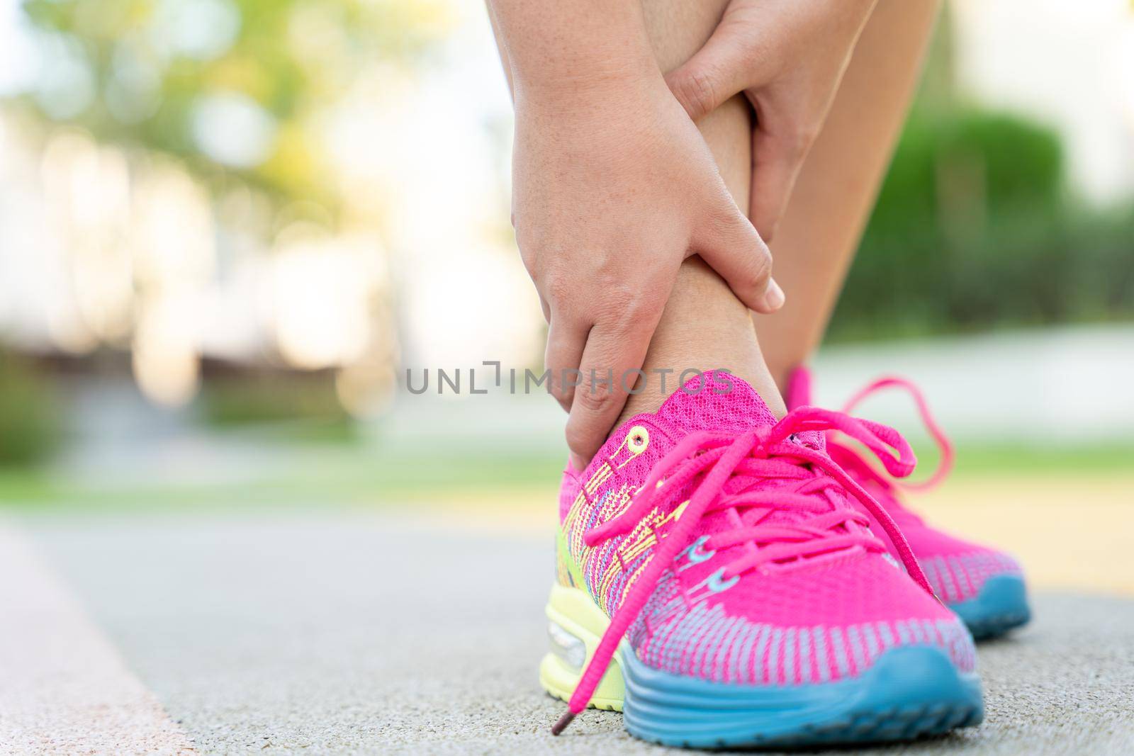 Female fatty runner athlete leg injury and pain. Hands grab painful ankle while running in the park. by mikesaran