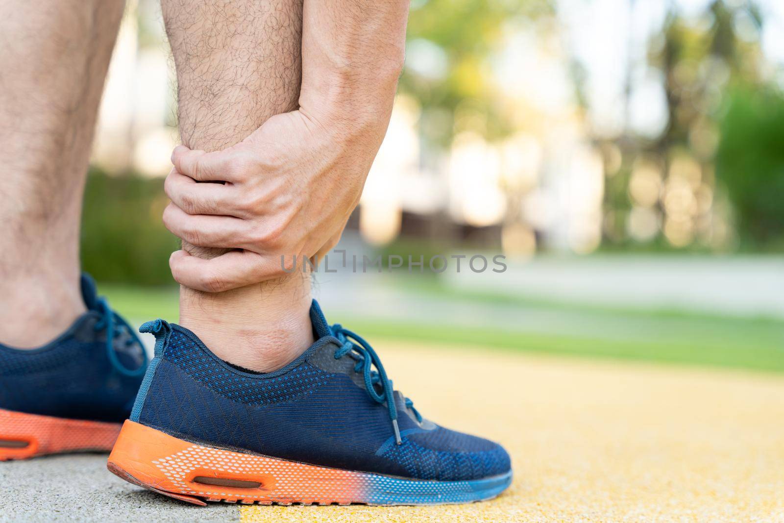 Male runner athlete leg injury and pain. Hands grab painful leg while running in the park.