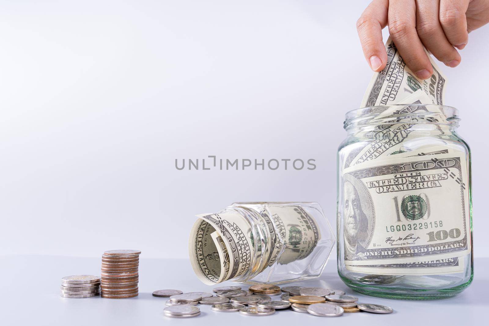 Hand putting money paper into jar with stack coins isolated grey background. Property investment and house mortgage financial concept.