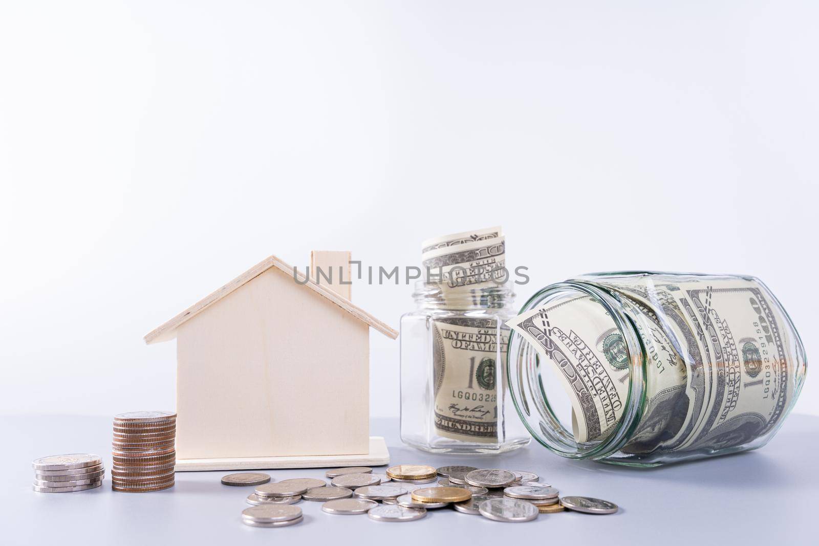 Money paper inside jar with wooden house and stack coins isolated grey background. Property investment and house mortgage financial concept.