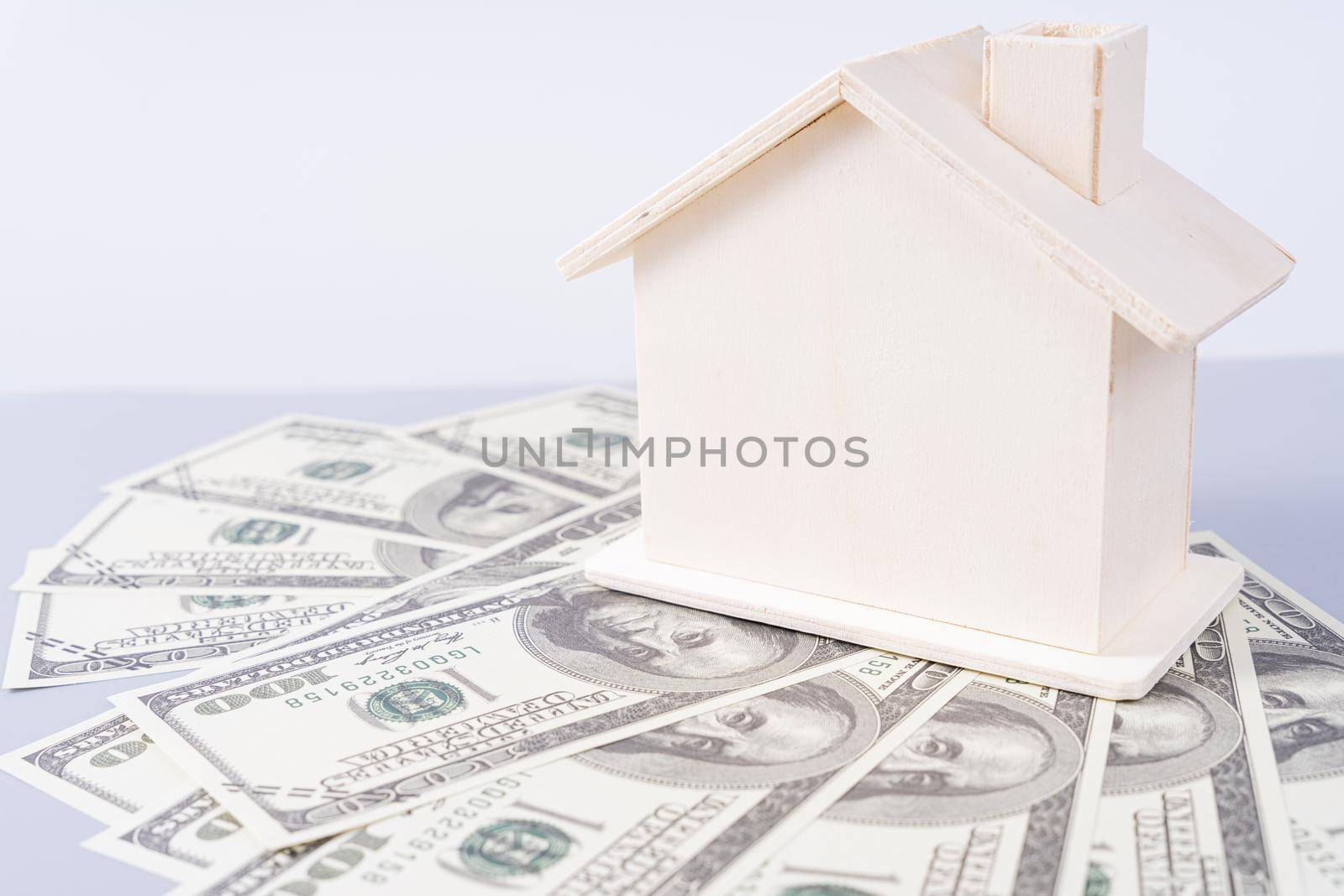 Wooden house and a pile of money paper isolated grey background. Property investment and house mortgage financial concept.