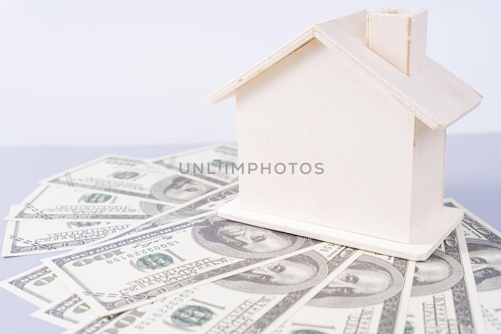Wooden house and a pile of money paper isolated grey background. Property investment and house mortgage financial concept.