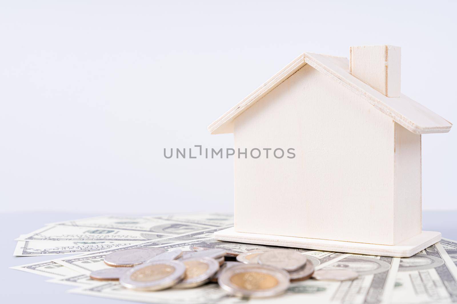 Wooden house and a pile of money coins and paper isolated grey background. Property investment and house mortgage financial concept. by mikesaran