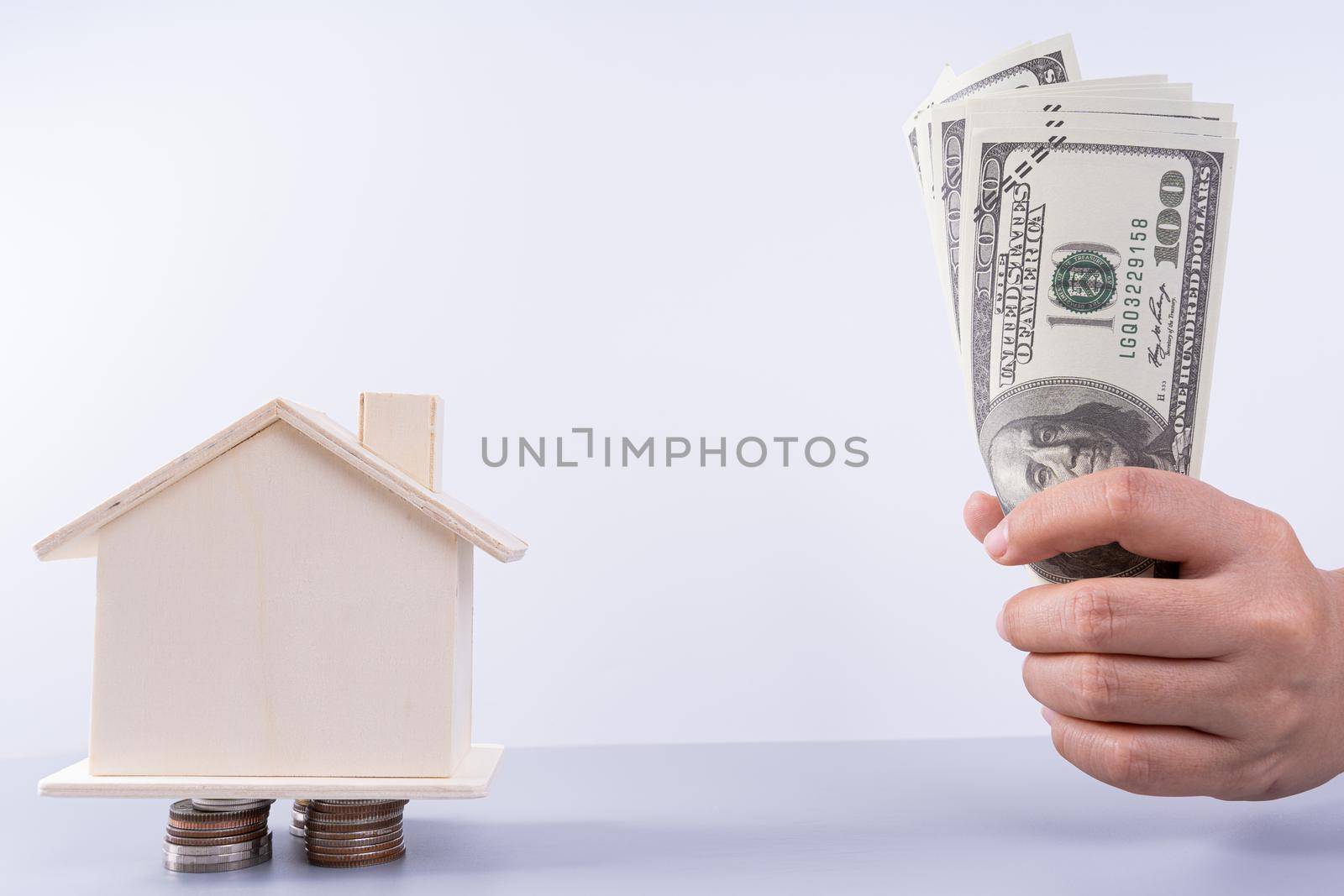 Hand holding money paper and wooden house on stack coins isolated grey background. Property investment and house mortgage financial concept.