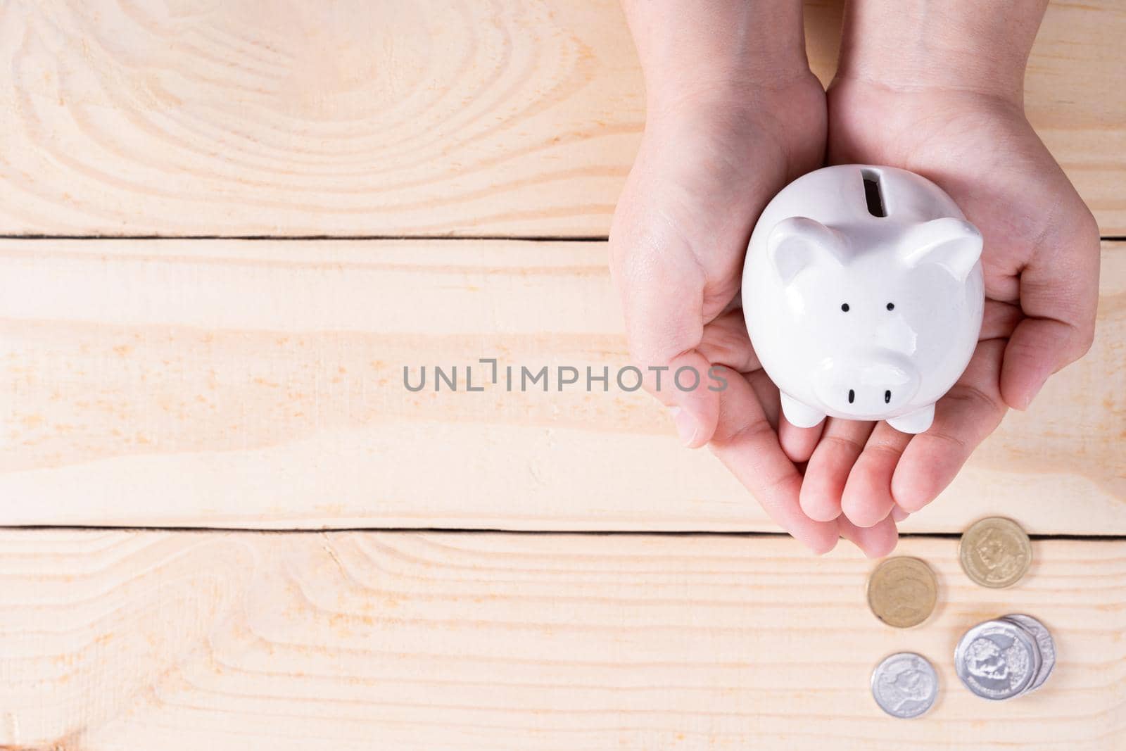 Hands hold a piggy bank with a pile of coins on wooden background. Saving money and investment concept.