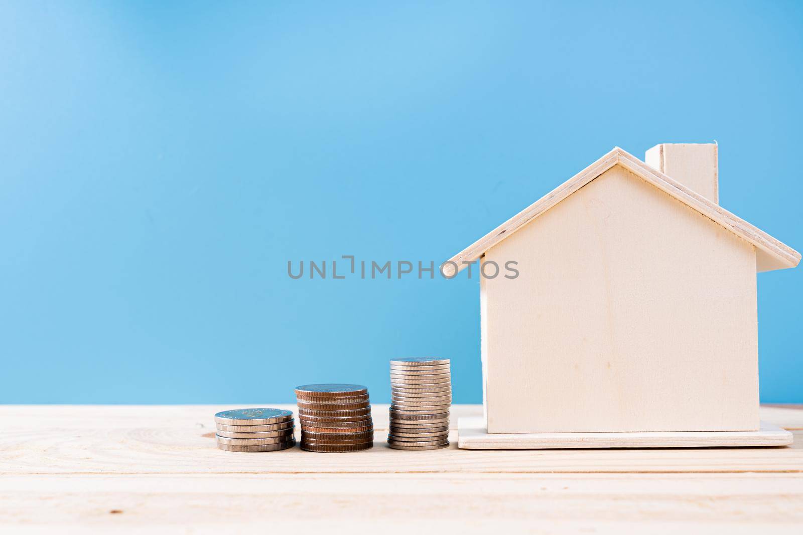 Wooden house with stack coins isolated blue background. Property investment and house mortgage financial concept.