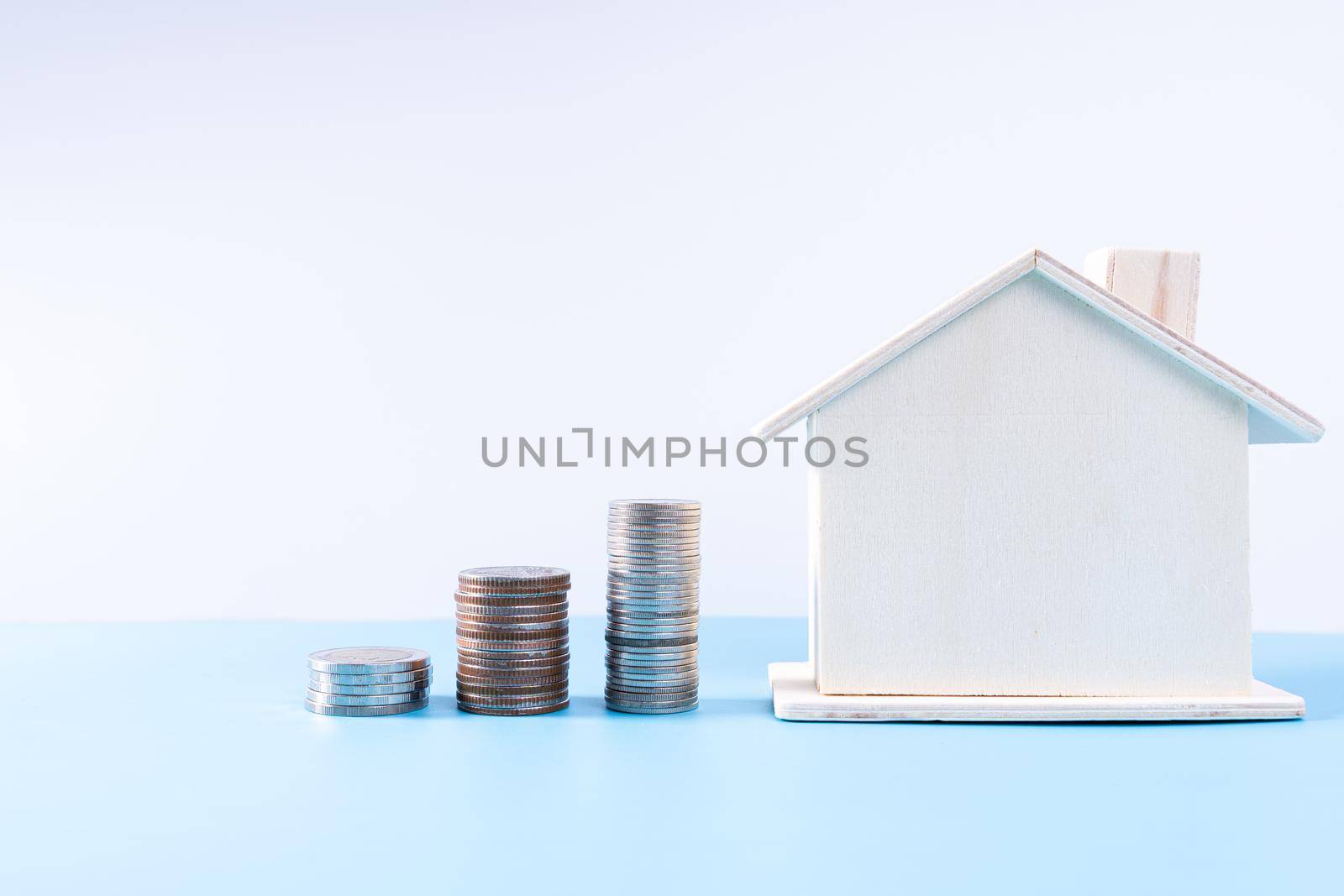 Wooden house with stack coins isolated grey background. Property investment and house mortgage financial concept. by mikesaran