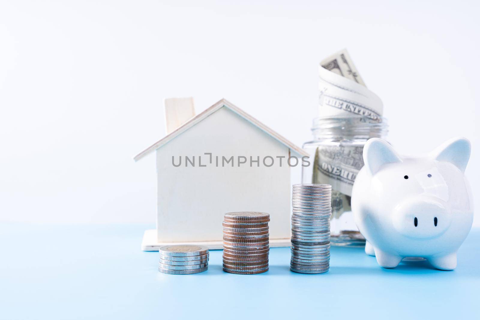 Piggy bank with wooden house and stack coins and money paper inside jar isolated grey background. Property investment and house mortgage financial concept. by mikesaran