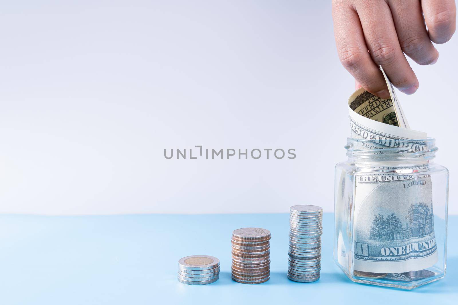 Hand putting money paper into jar with stack coins isolated grey background. Property investment and house mortgage financial concept. by mikesaran