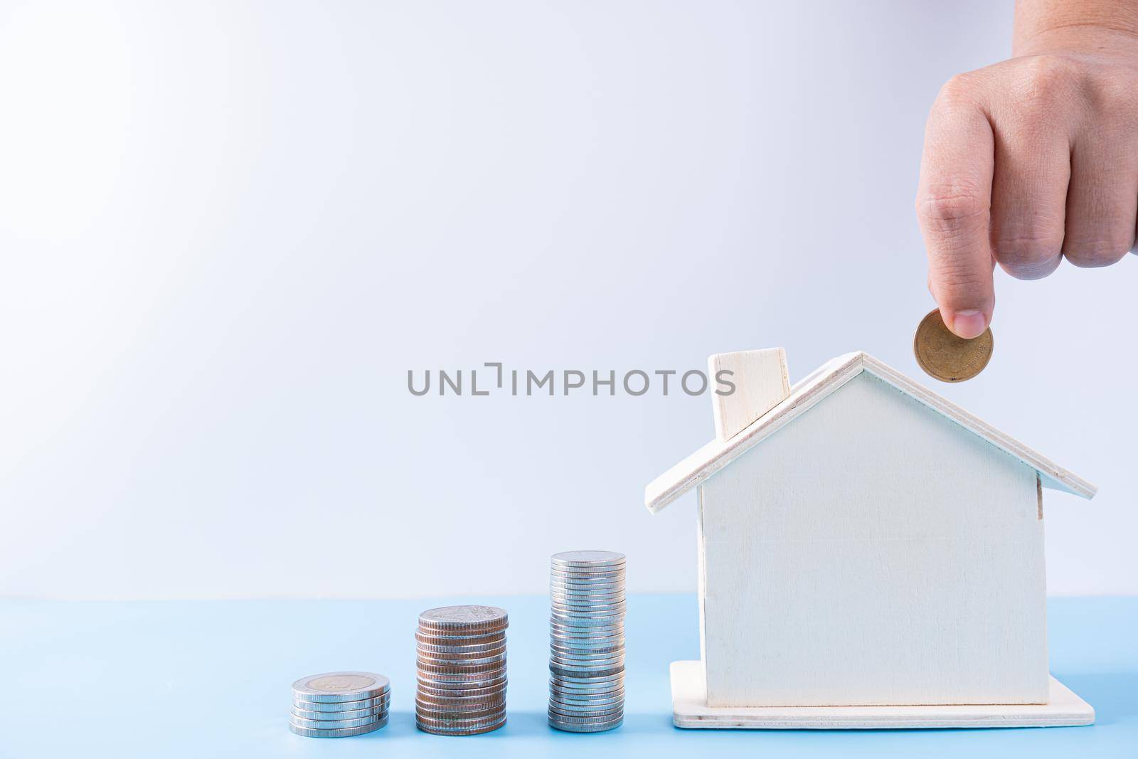 Hand putting money coin into wooden house with stack coins isolated grey background. Property investment and house mortgage financial concept. by mikesaran