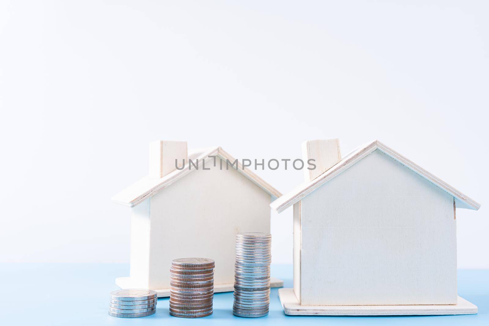 Wooden house with stack coins isolated grey background. Property investment and house mortgage financial concept. by mikesaran