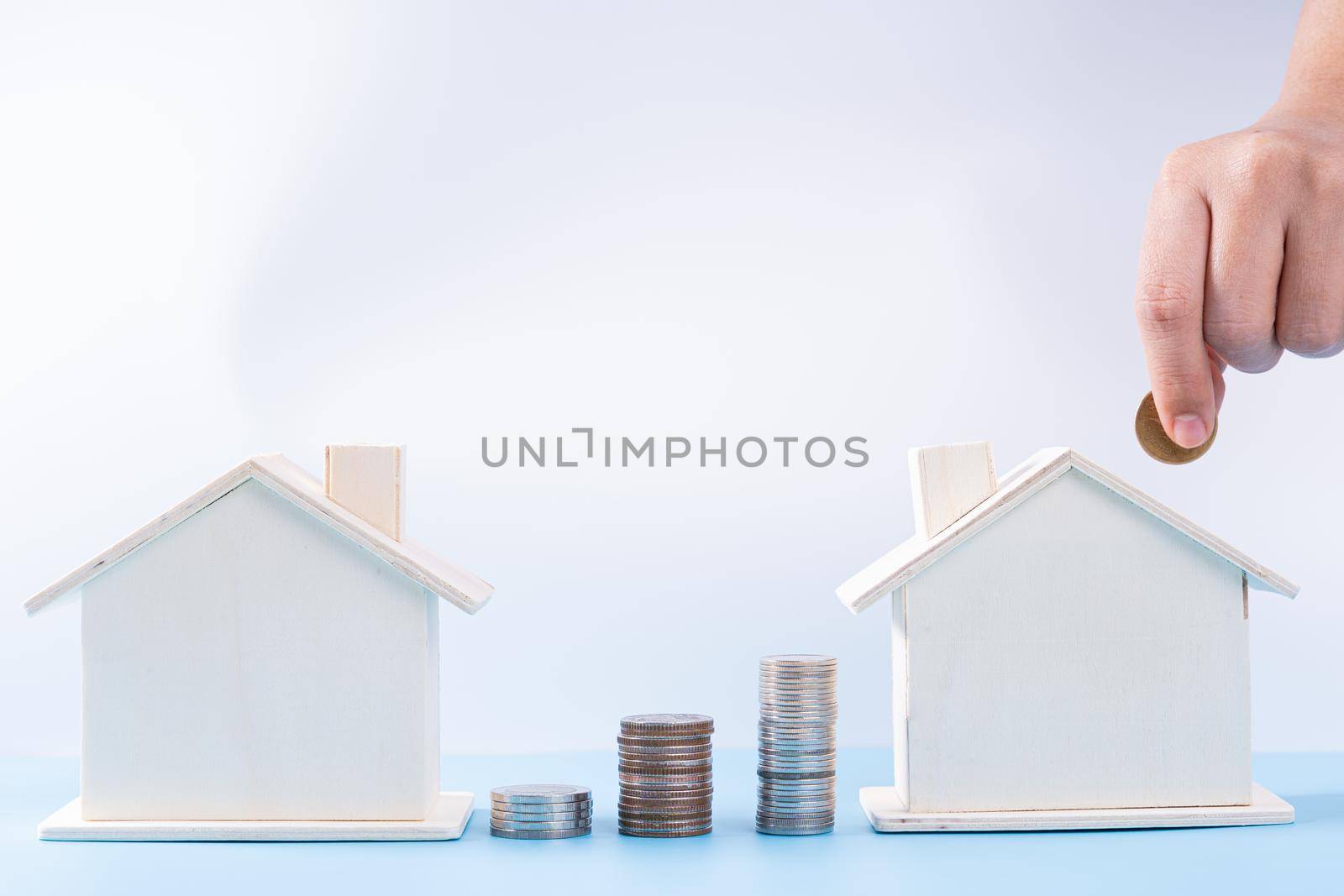 Hand putting money coin into wooden house with stack coins isolated grey background. Property investment and house mortgage financial concept.