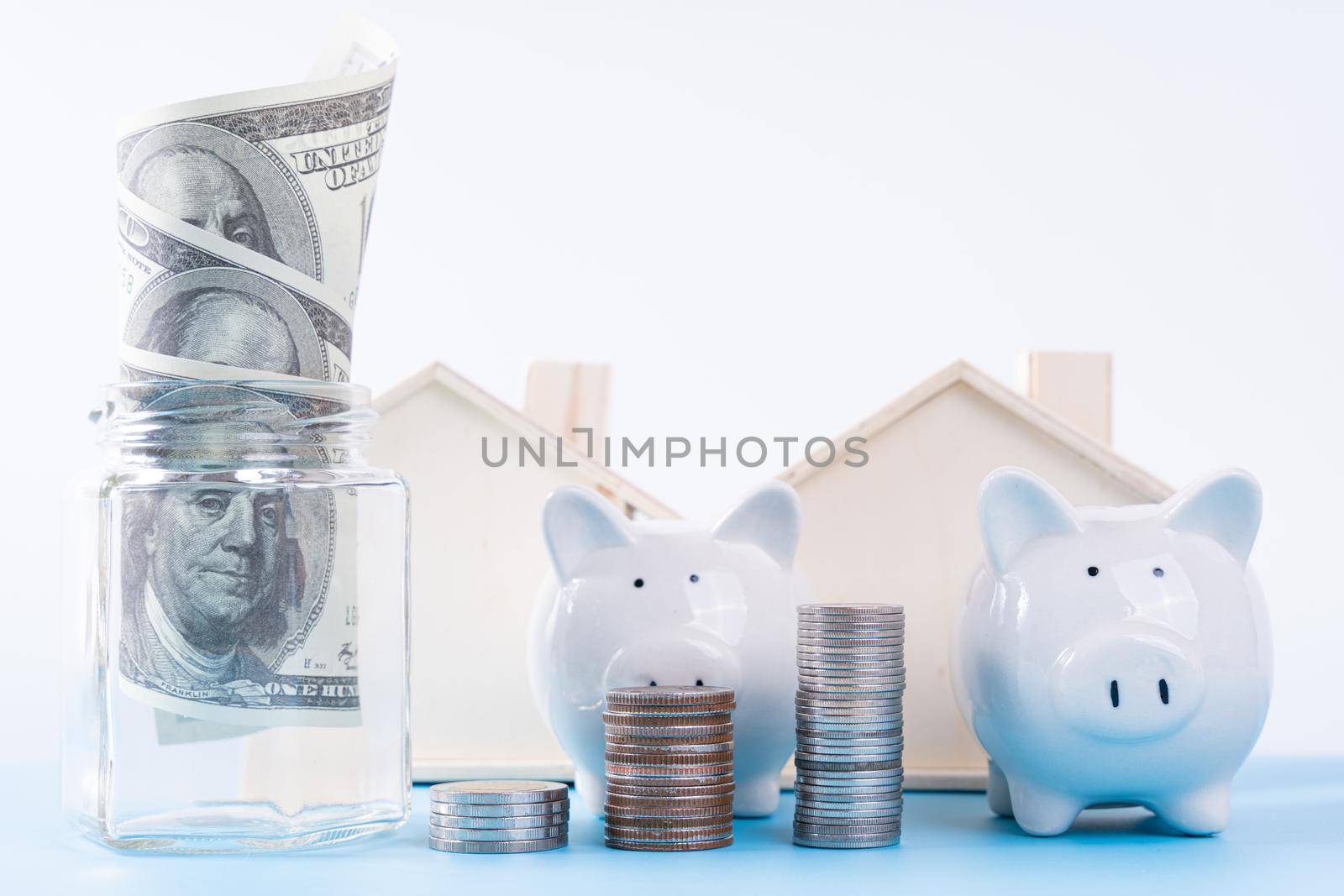 Piggy bank with stack coins and money paper inside jar and wooden house isolated grey background. Property investment and house mortgage financial concept.