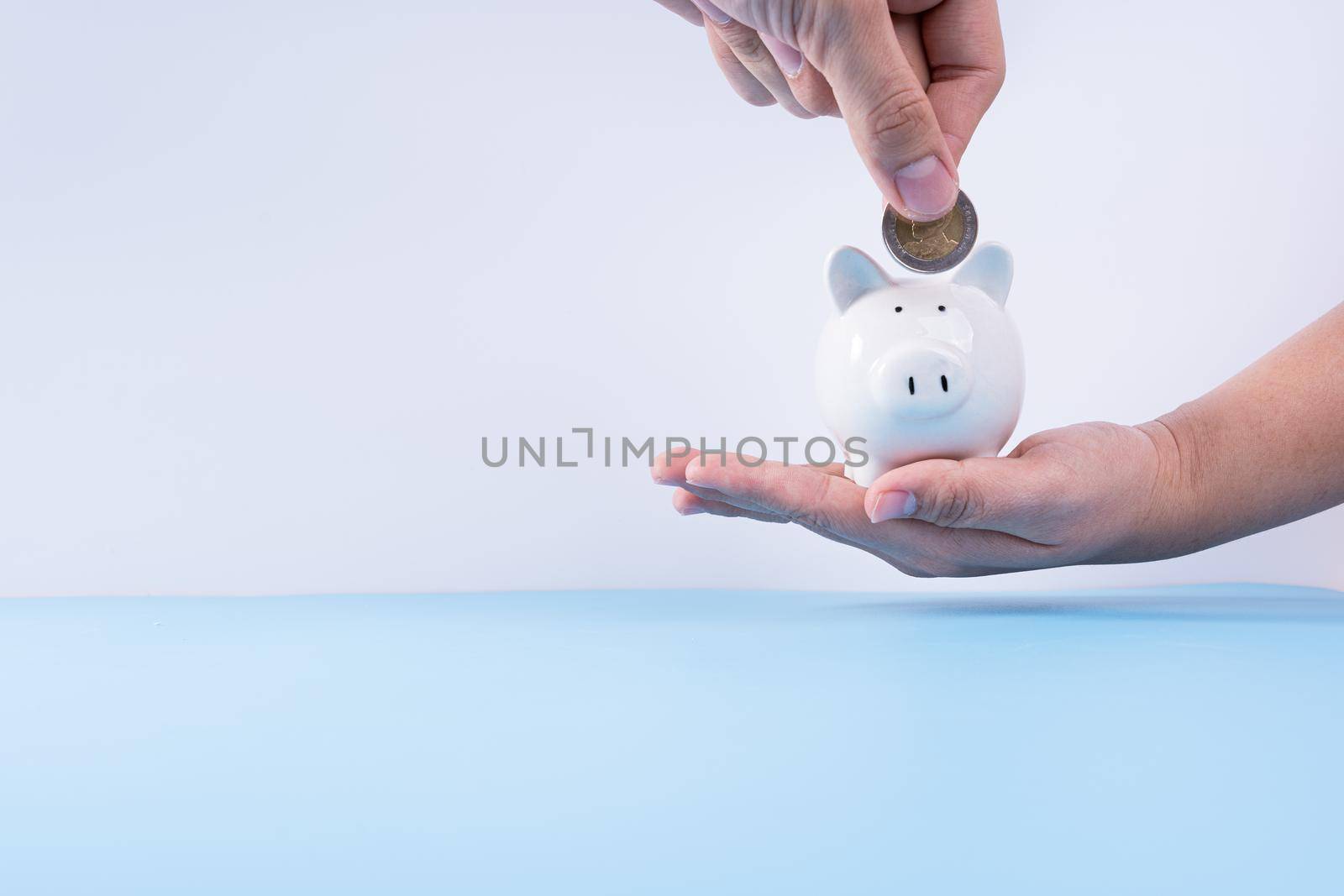 Hand putting money coin into piggy bank isolated grey background. Property investment and house mortgage financial concept. by mikesaran