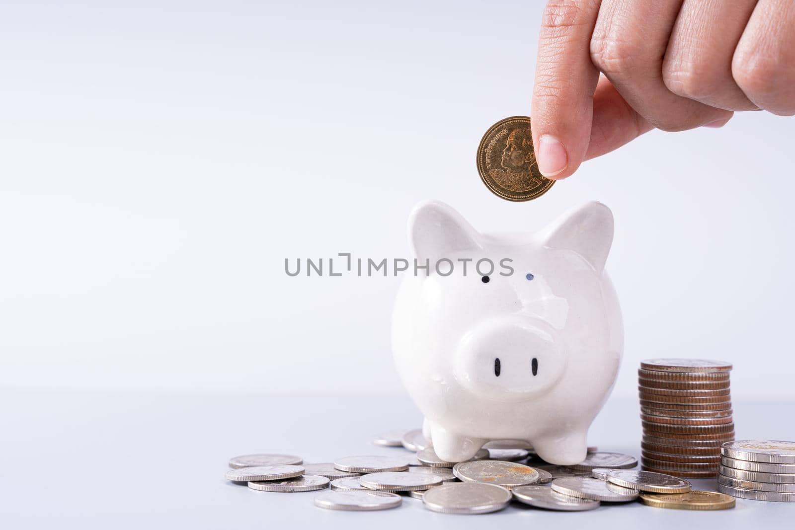 Hand putting money coin into piggy bank with stack coins isolated grey background. Saving money and investment concept.