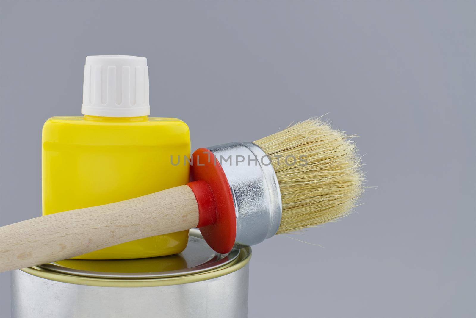 Clean bristle brush and yellow pigment jar on tin of paint over a grey background. New color, decorating or renovations concept