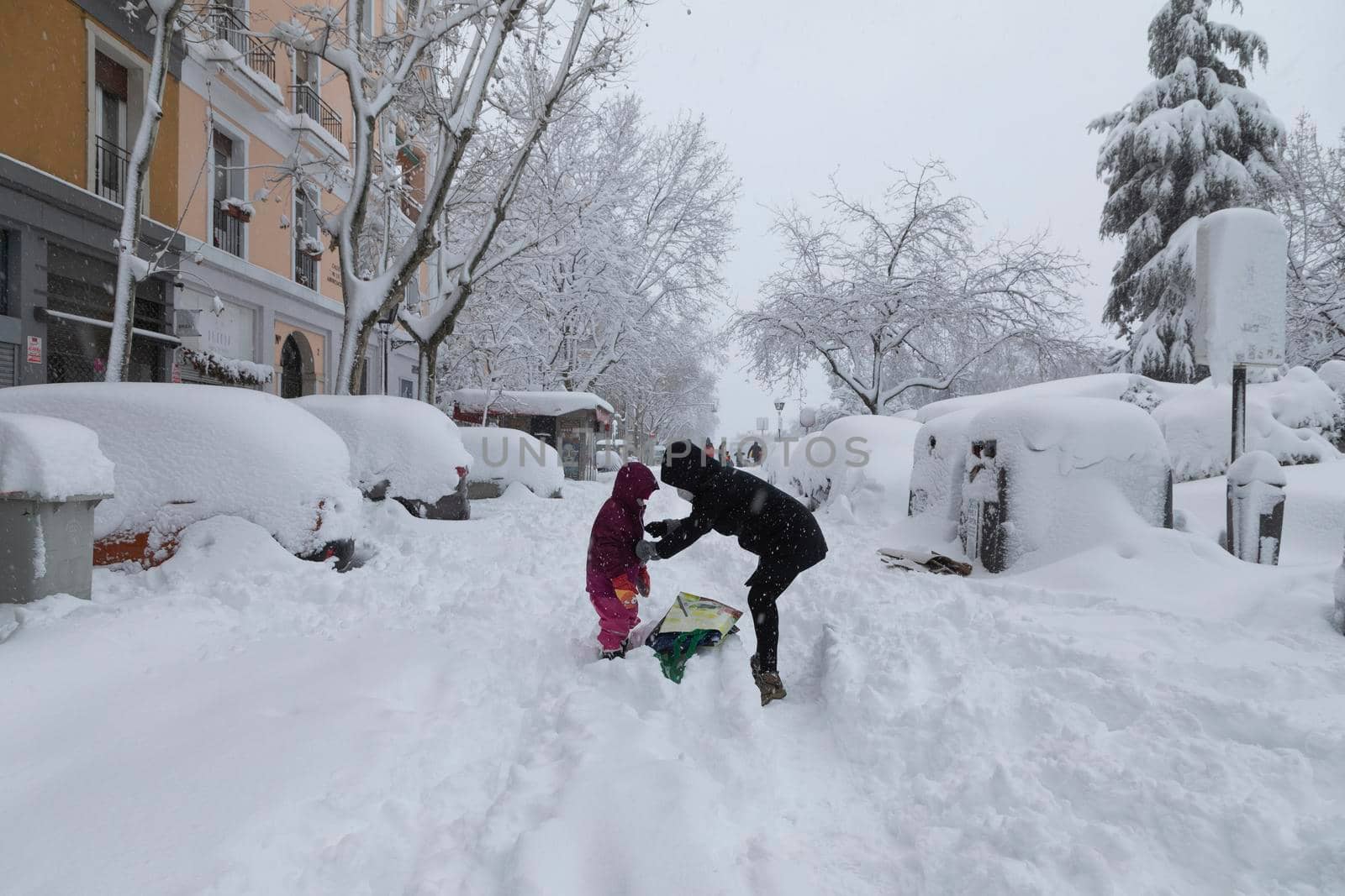 Mother zips up her daughter on a snowy day, Madrid. by alvarobueno